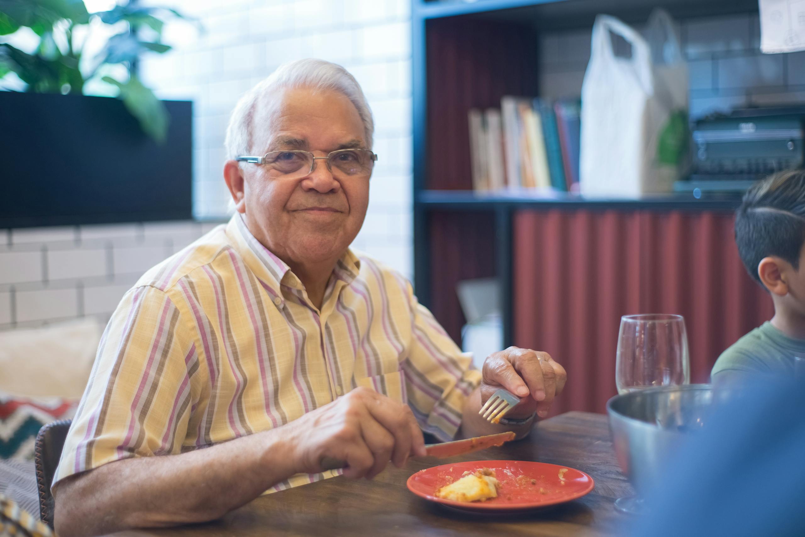 Senior man in a striped shirt smiling while dining indoors.