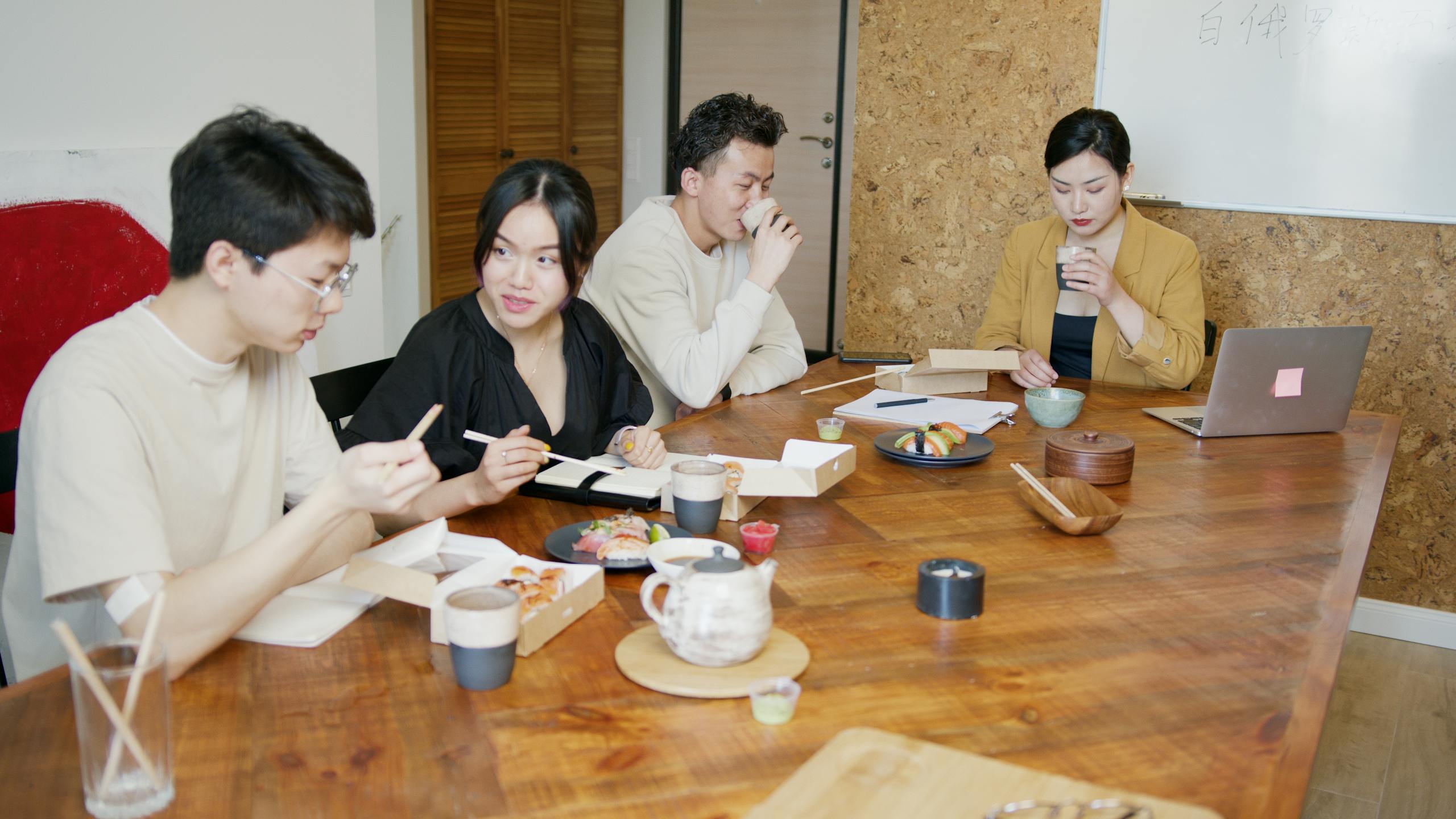 Team sharing sushi lunch around a wooden table in a contemporary office setting.