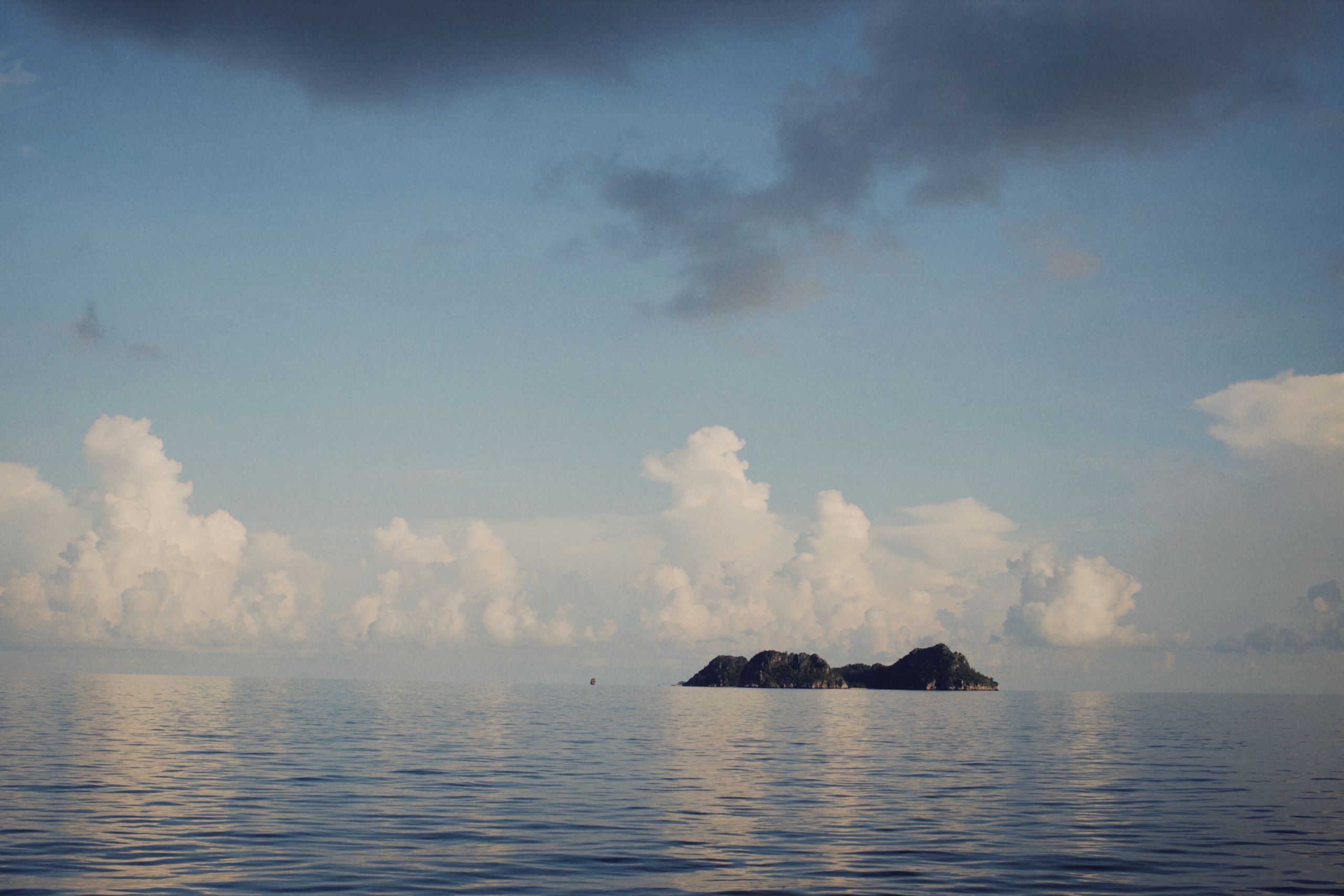 Tranquil scene of a solitary island surrounded by a calm sea and dramatic cloud formations.