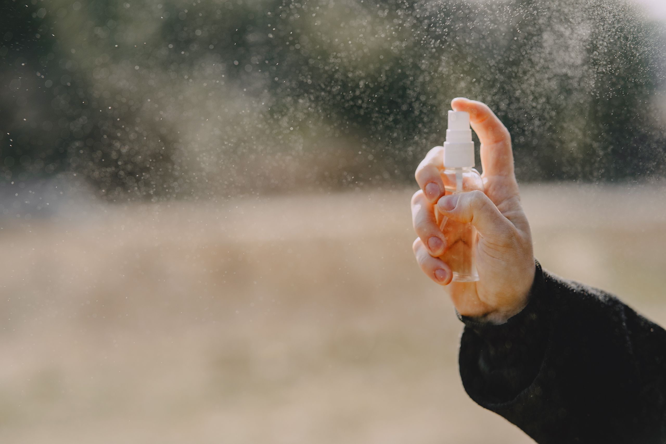 Unrecognizable man in casual wear showing bottle with liquid and spraying water outdoors
