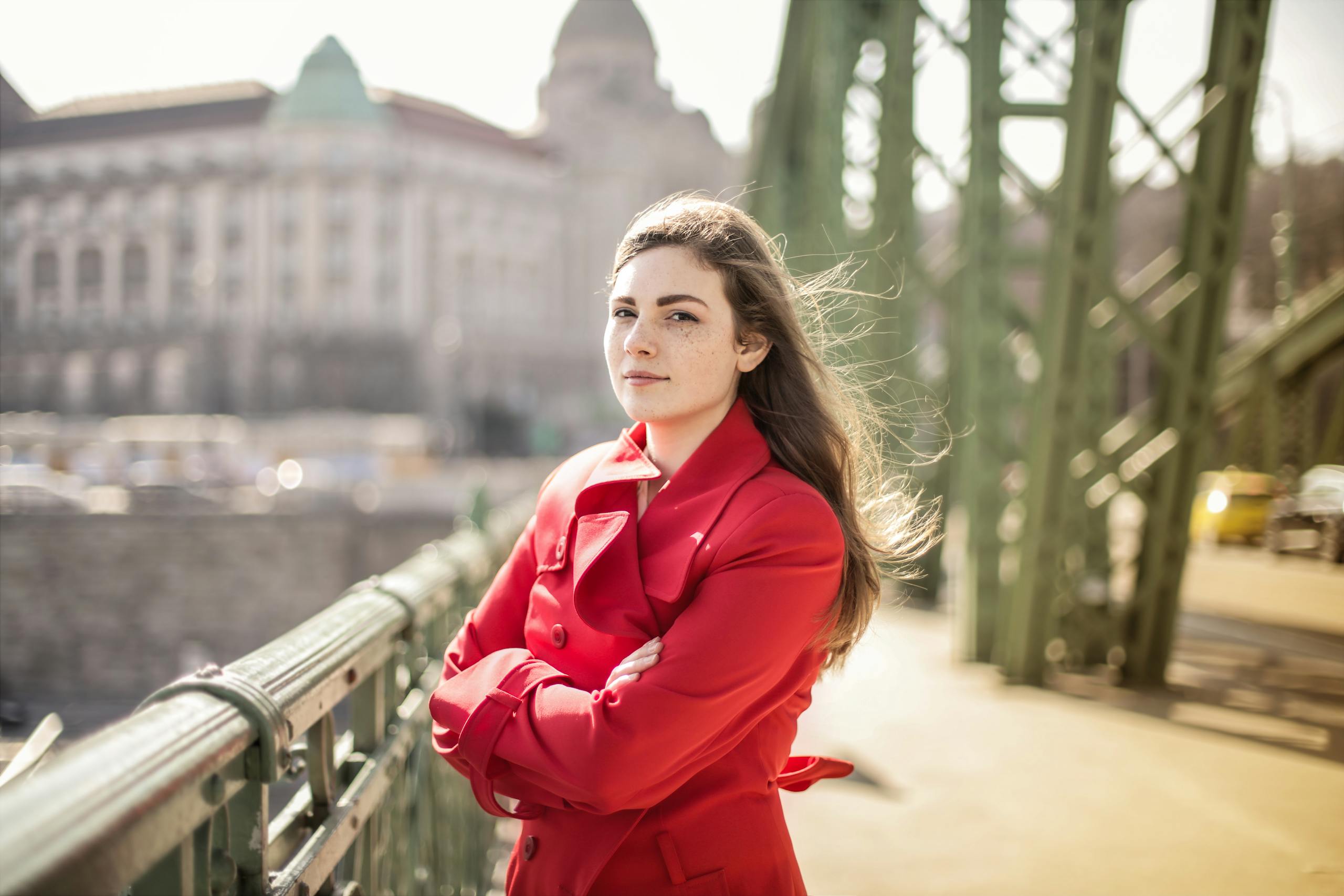 Woman in a red coat standing confidently on a bridge on a windy day.