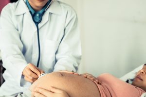 Happy pregnant woman visit gynecologist doctor at hospital or medical clinic for pregnancy consultant. Doctor examine pregnant belly for baby and mother healthcare check up. Gynecology concept.