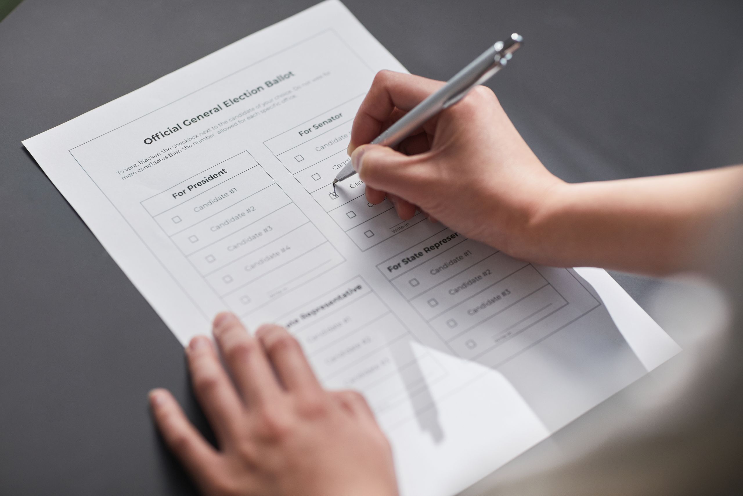 A close-up image of a hand marking an official election ballot with a pen, representing democratic voting.