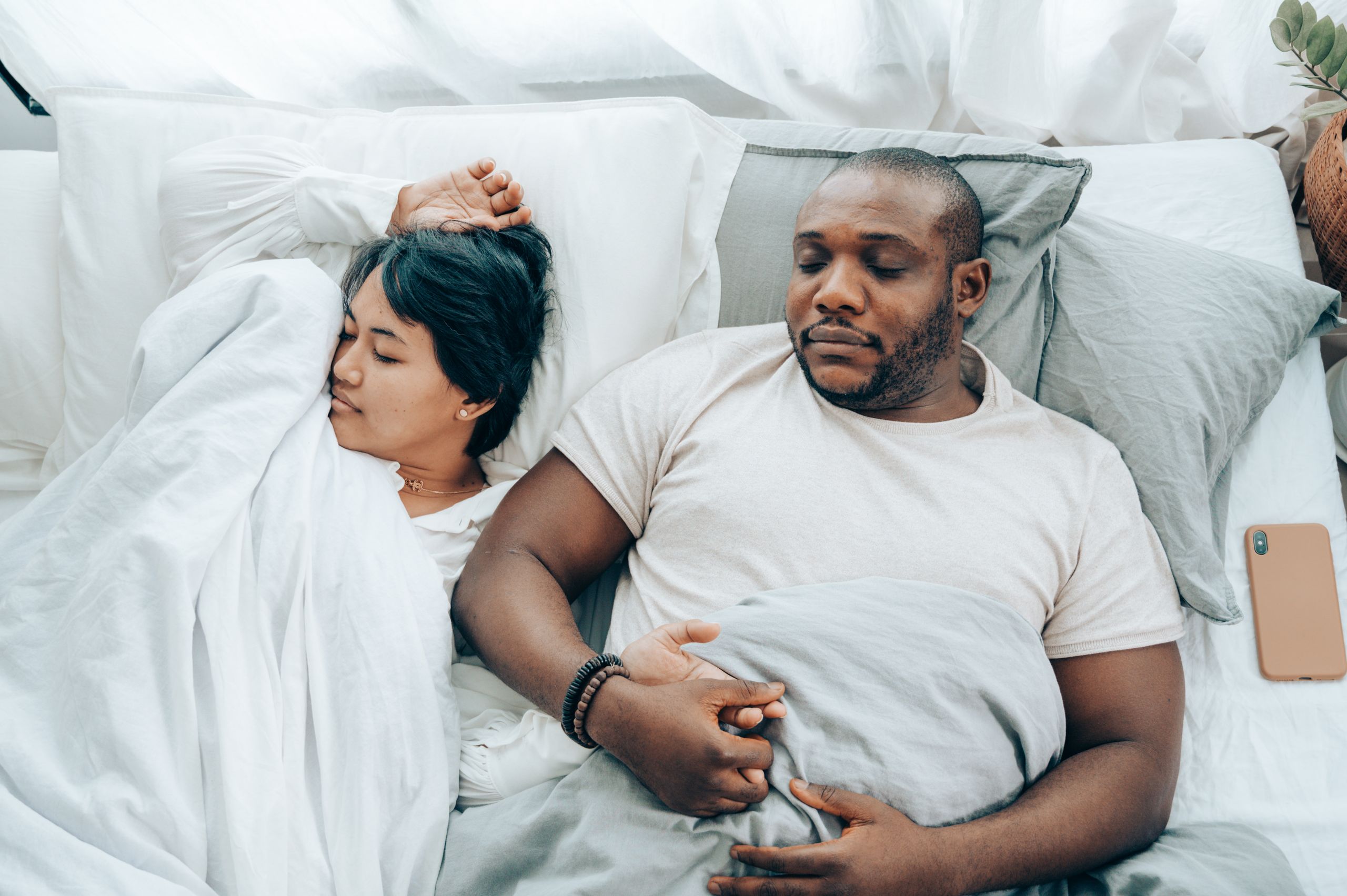 From above of romantic diverse couple holding hands while sleeping in comfortable bed at home in morning