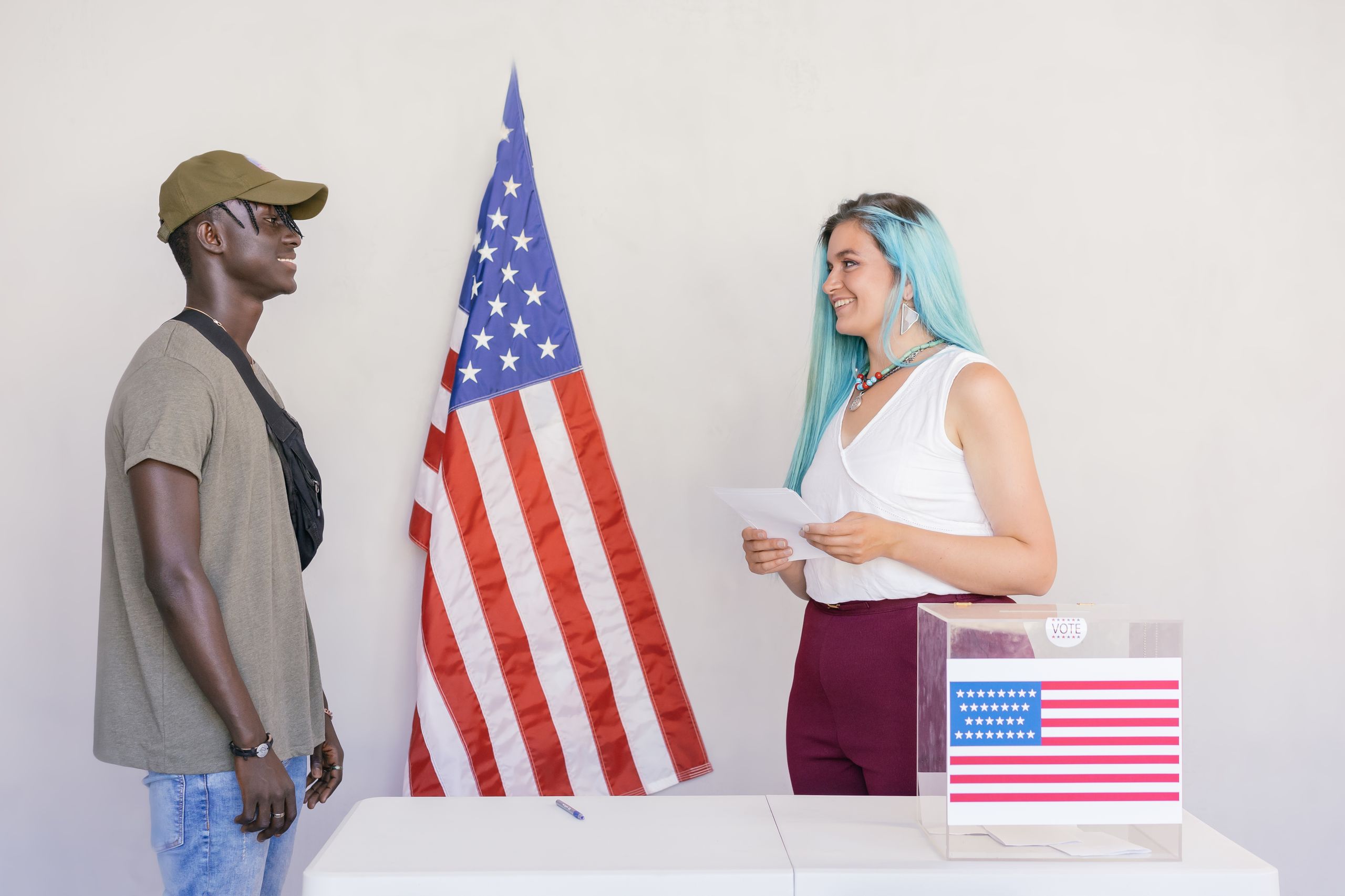 Two diverse young adults engaging in a voting process next to an American flag.