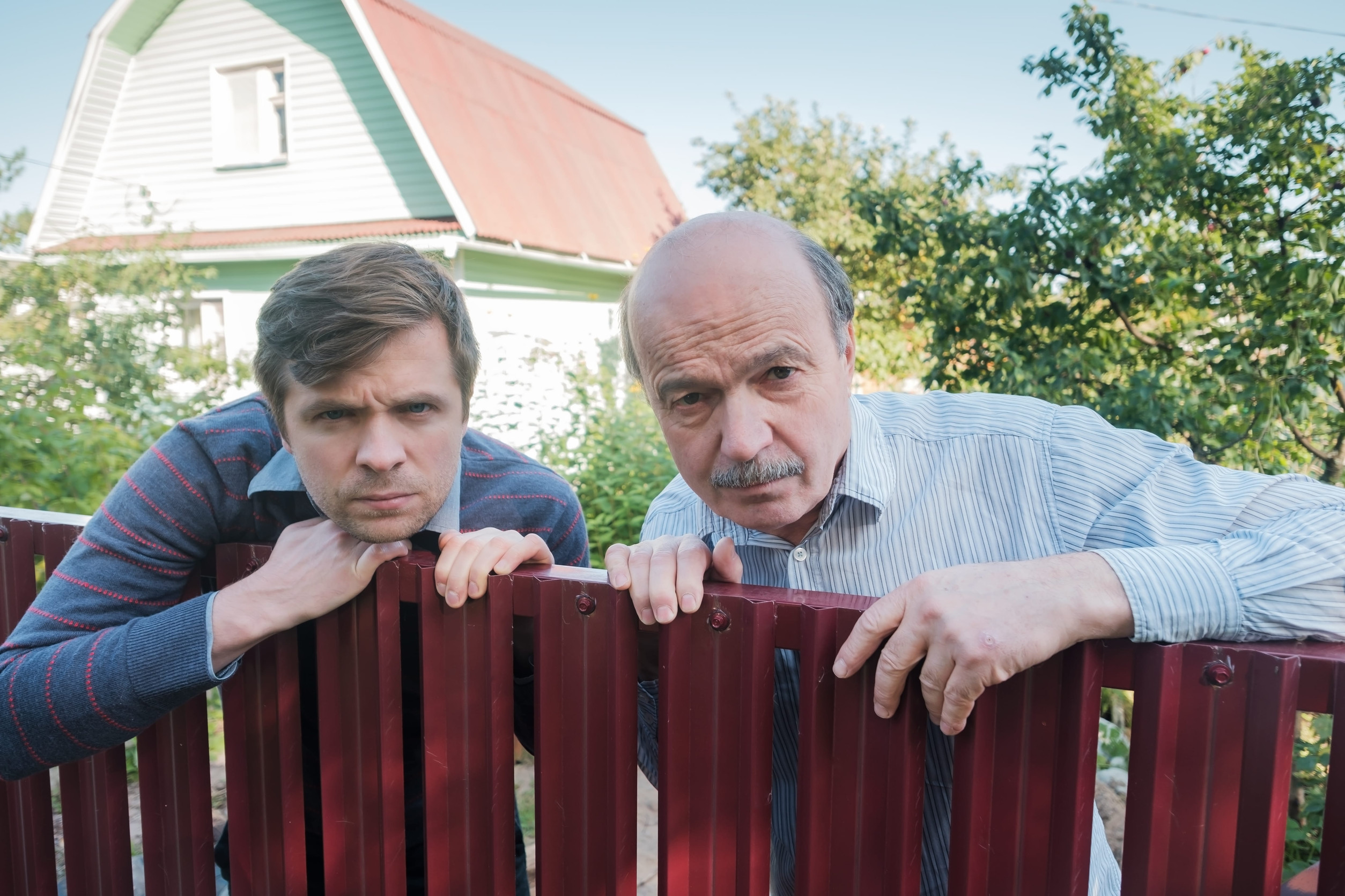 two angry caucasian men carefully watching over the fence. Concept of curious neighbors and private life