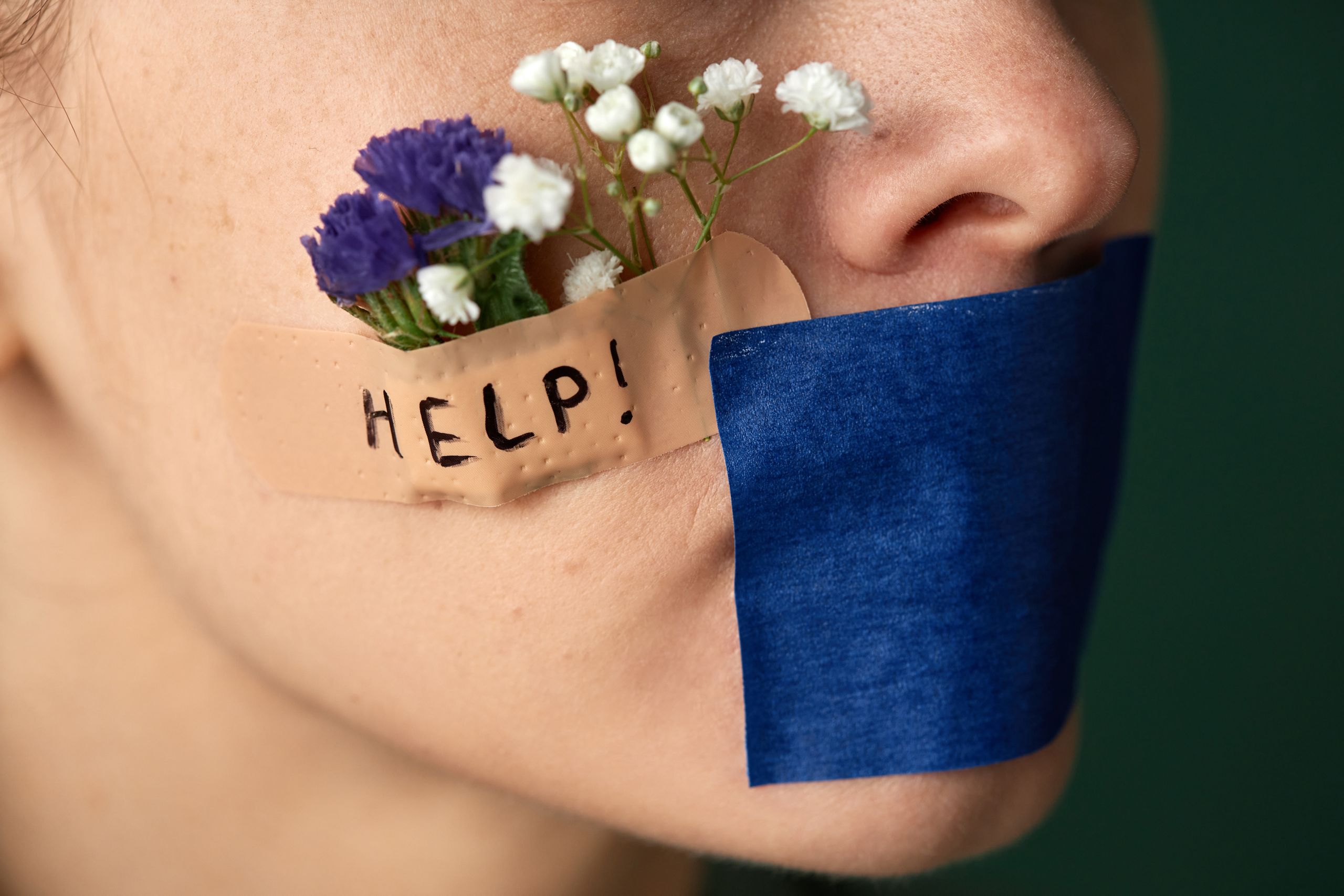 A conceptual image featuring flowers and tape on a face symbolizing silence and a cry for help.