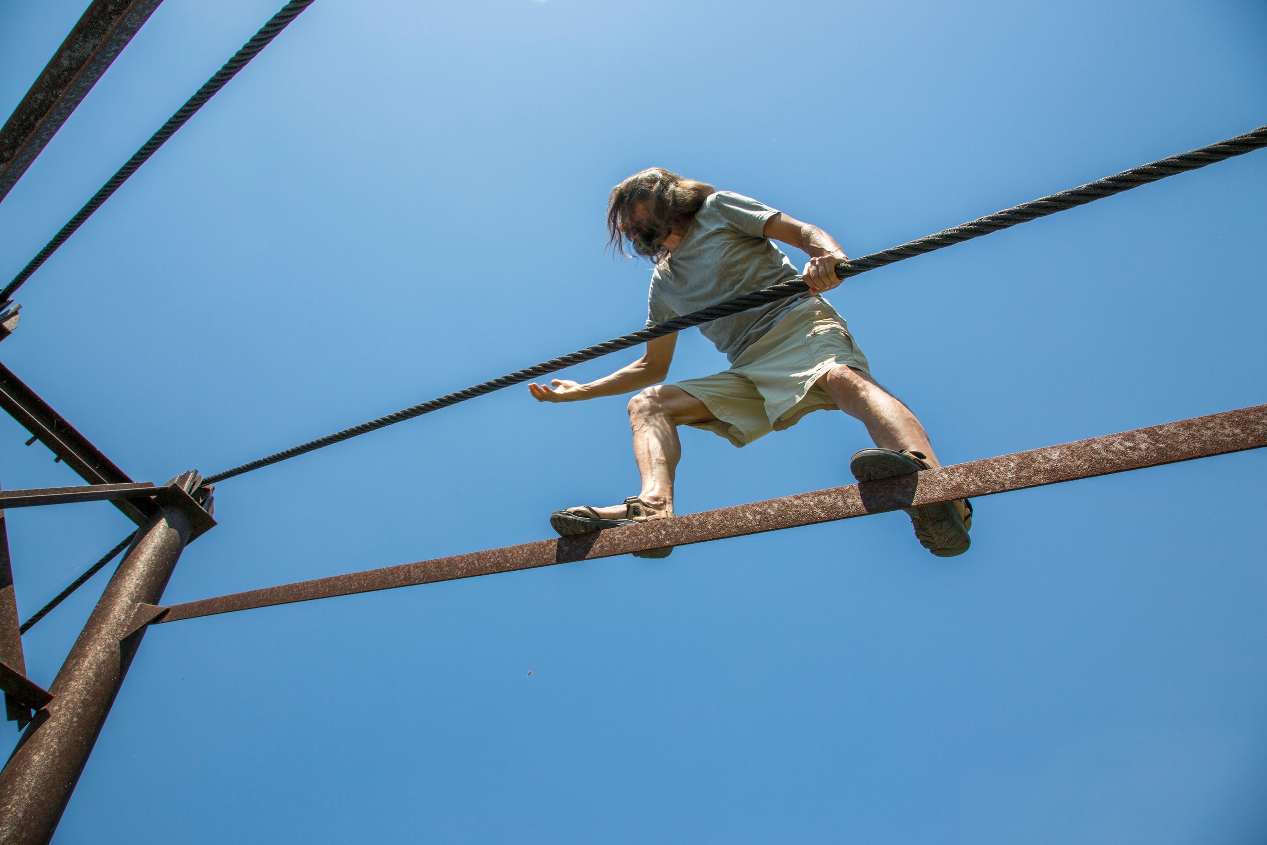 A man skillfully balances on a high wire against a bright blue sky, showcasing adventure and balance.
