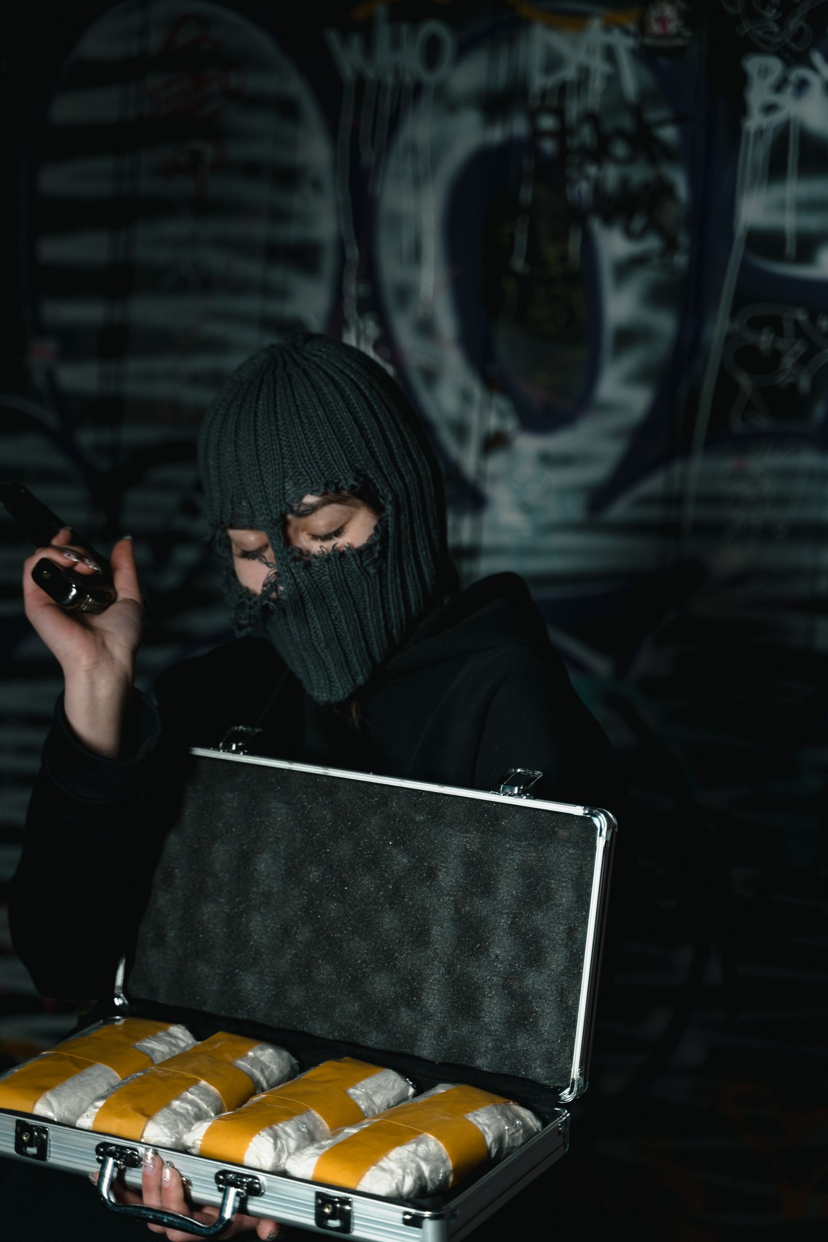 A masked individual holding a briefcase with wrapped packages, evoking crime and secrecy.