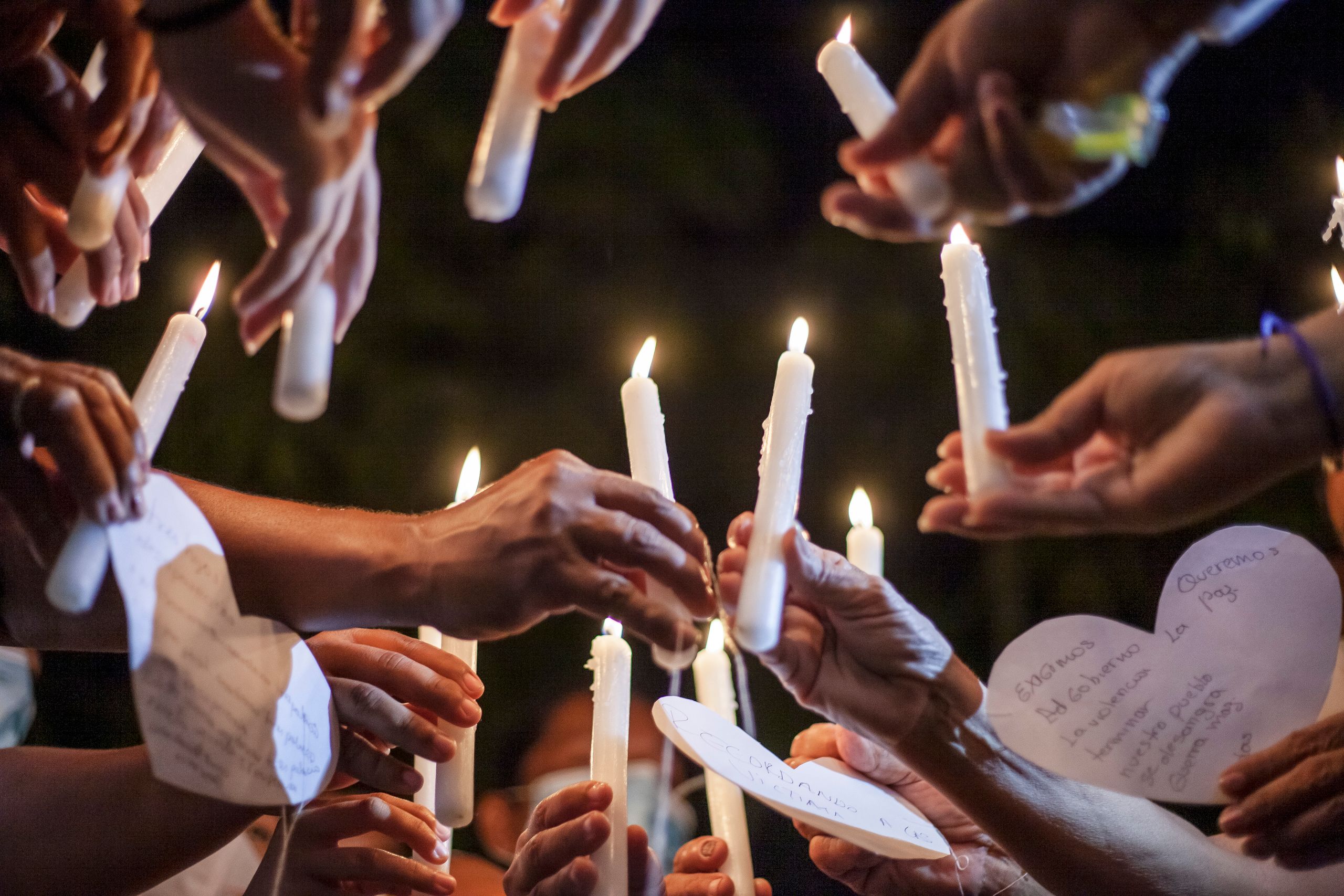 Candlelight vigil with hands holding candles and heart-shaped messages at night in Ovejas, Colombia.