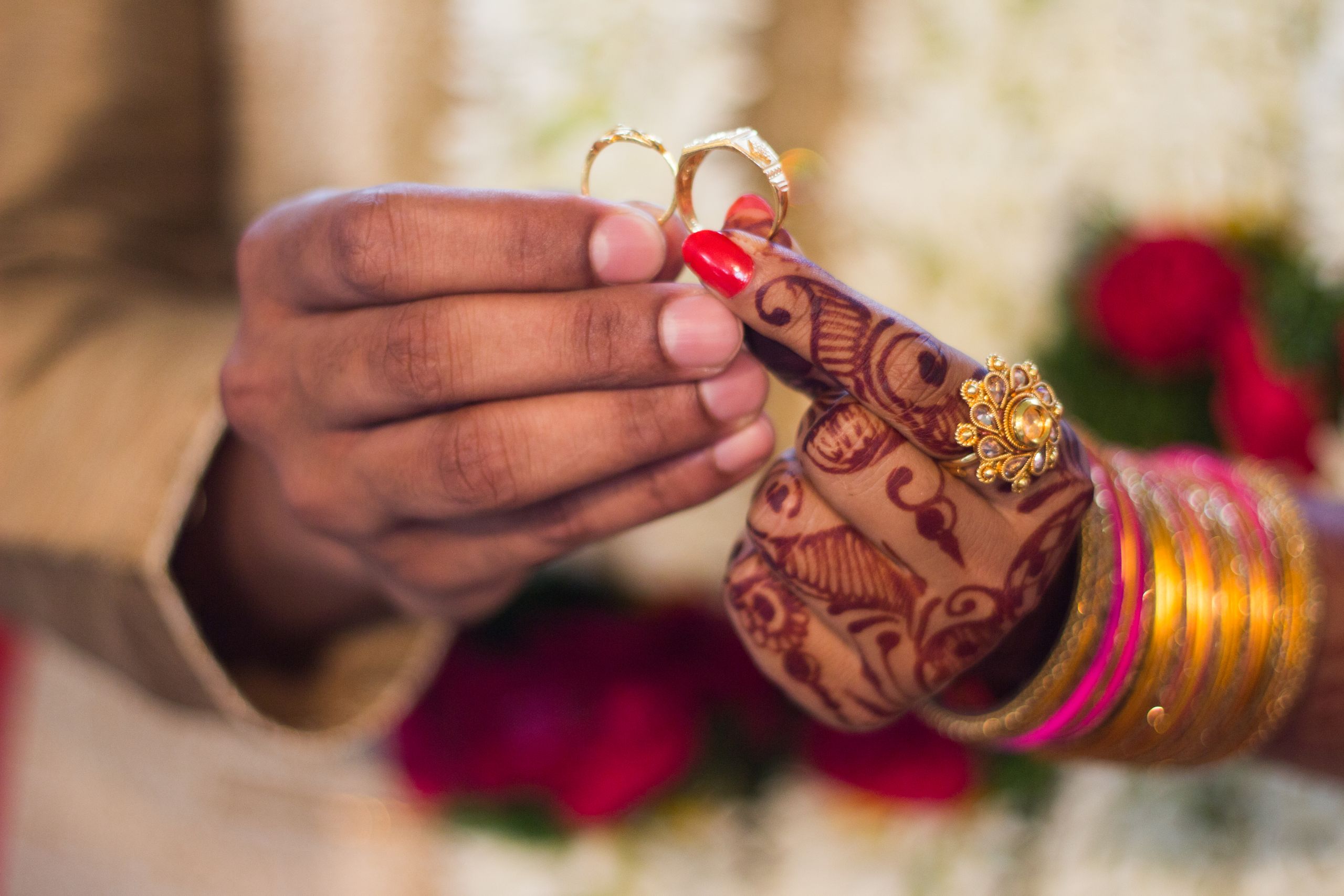 Close-up of hands with henna and jewelry during a traditional Indian wedding ceremony, exchanging rings.