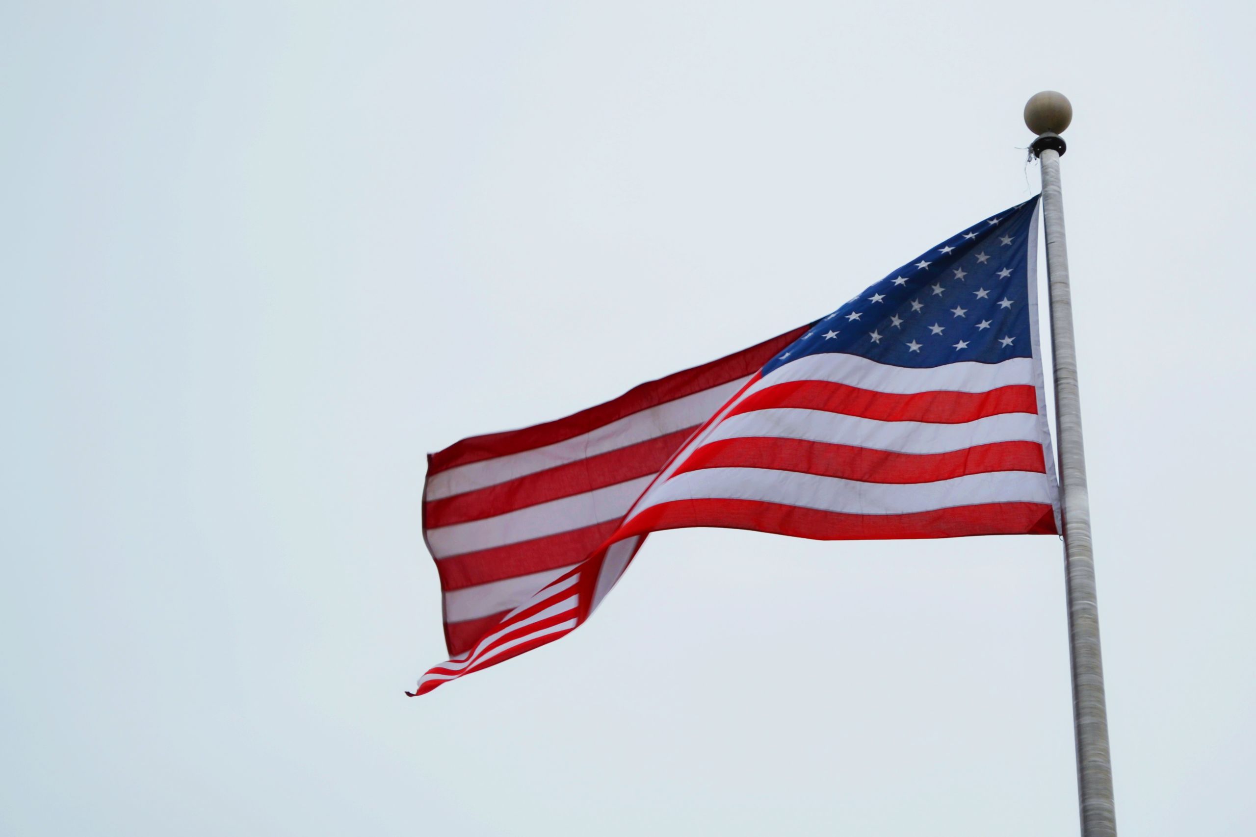USA flag on pole with clear sky, symbolizing freedom and patriotism.