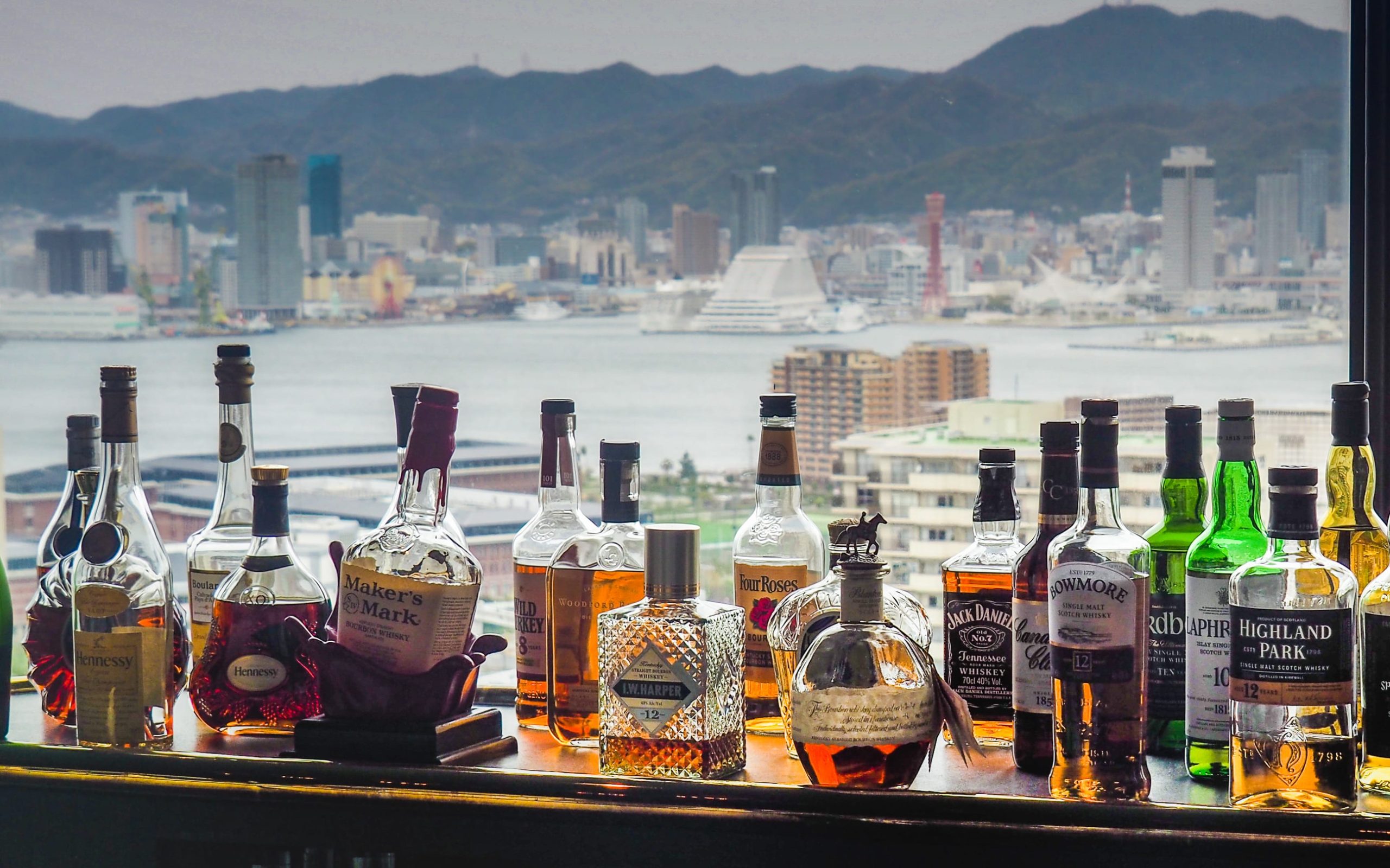 JAPAN, KOBE - APRIL 11, 2017: whiskey bottles on bar counter with blurred Kobe tower and city skyline blurred in background.