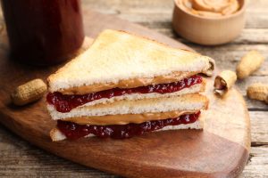 Tasty sandwiches with peanut butter, jam and nuts on wooden table, closeup