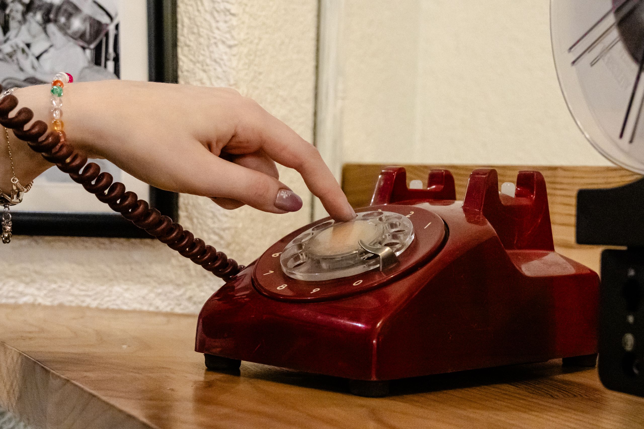 A close-up of a hand dialing a classic red rotary phone, capturing nostalgia.