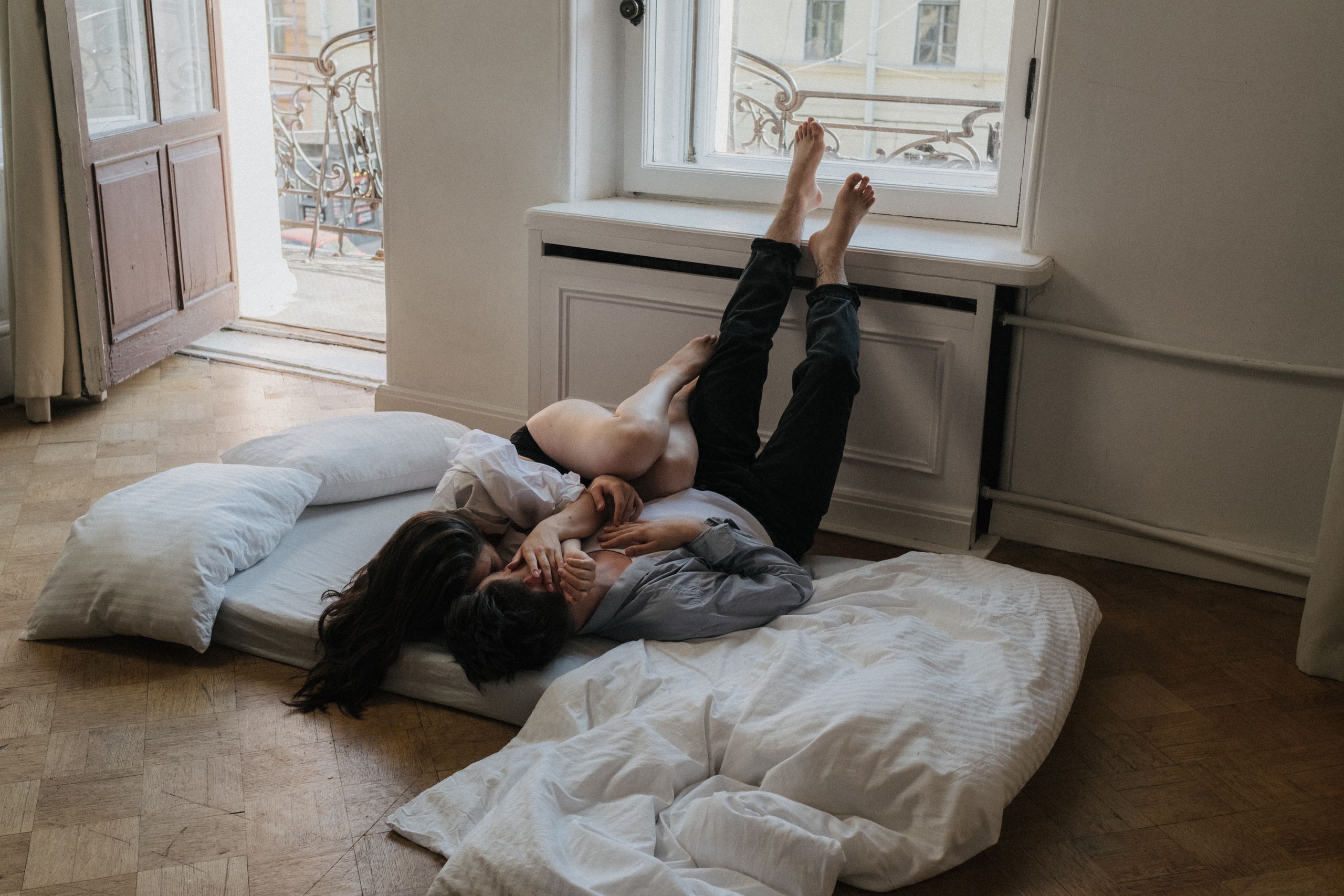 A couple lying on a mattress near a window, enjoying a relaxed and affectionate moment indoors.