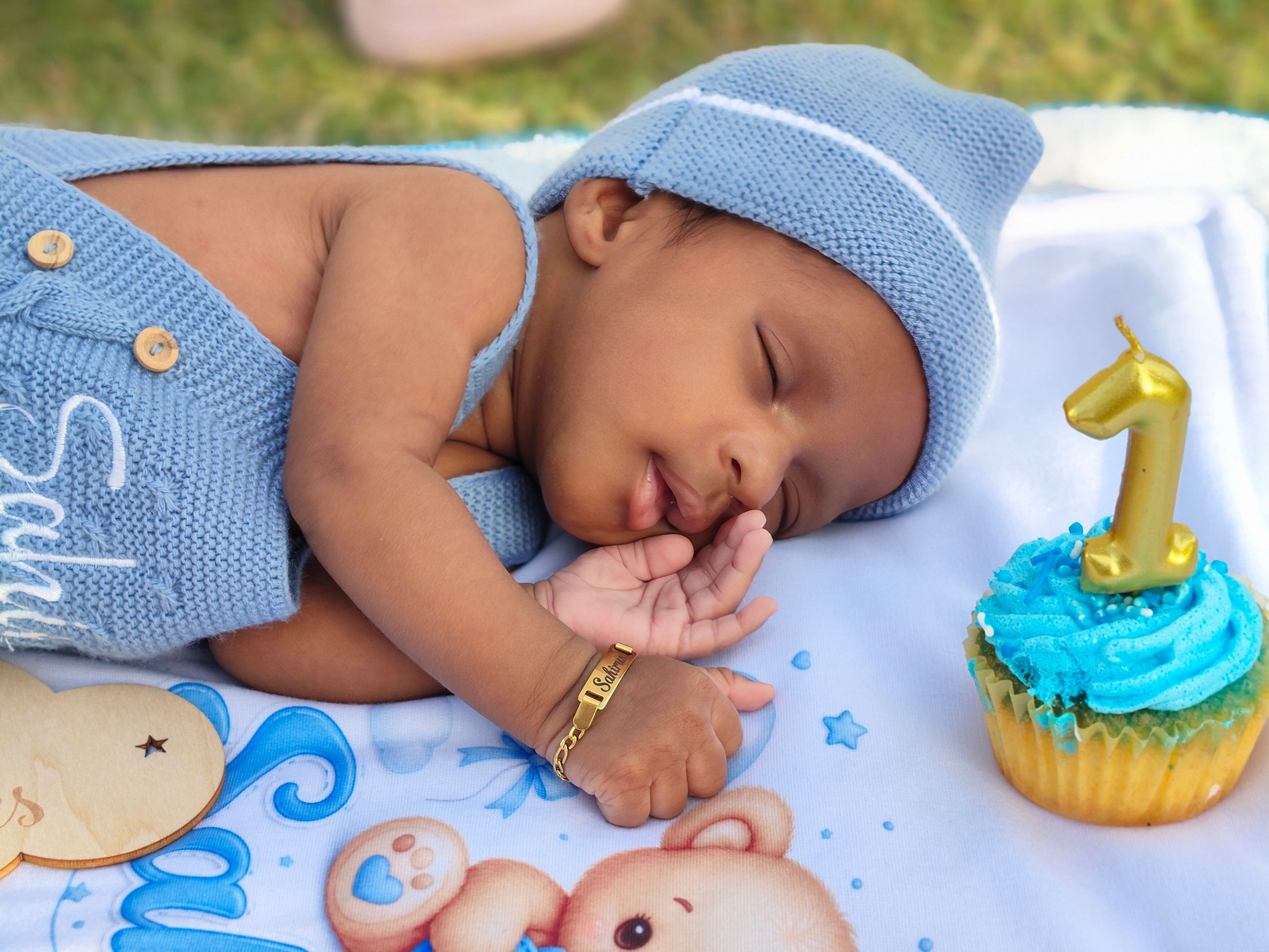 A cute baby sleeping beside a cupcake with a candle shaped like the number one, celebrating first birthday.