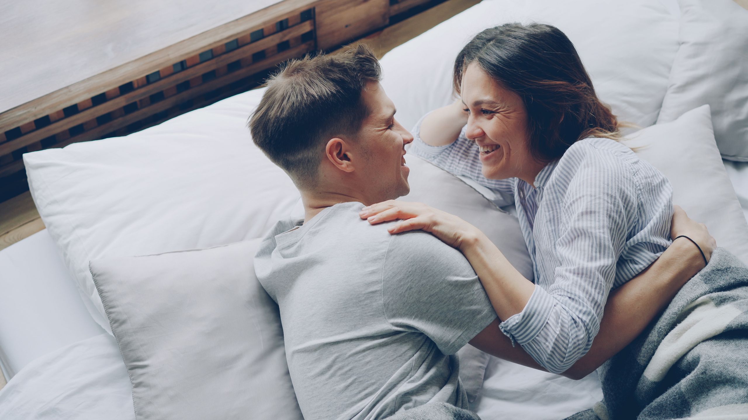 A joyful moment of a couple laughing and embracing on a bed, conveying love and happiness.