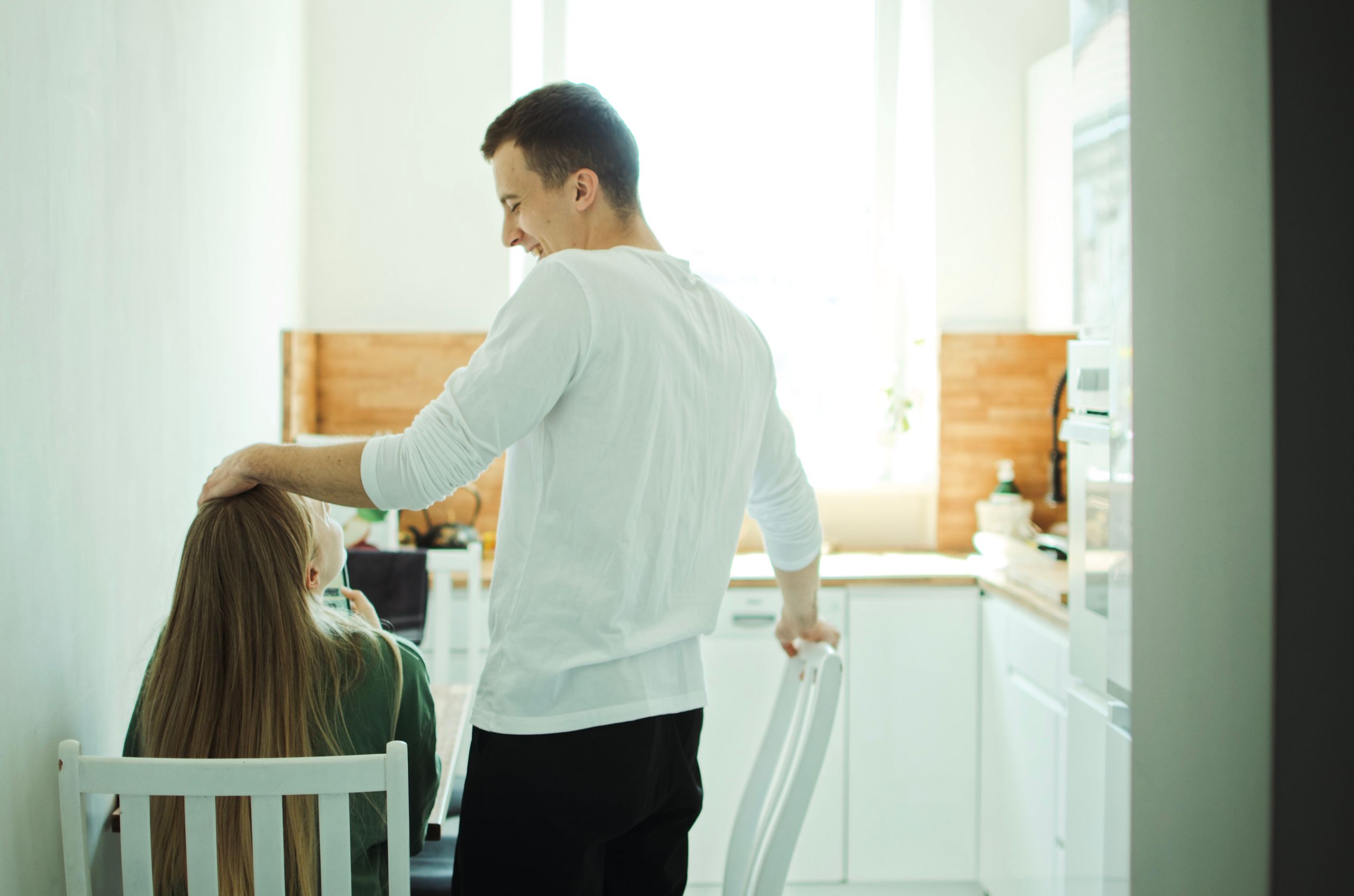 A man gently pats a woman's head in a bright kitchen, capturing a moment of casual bonding.