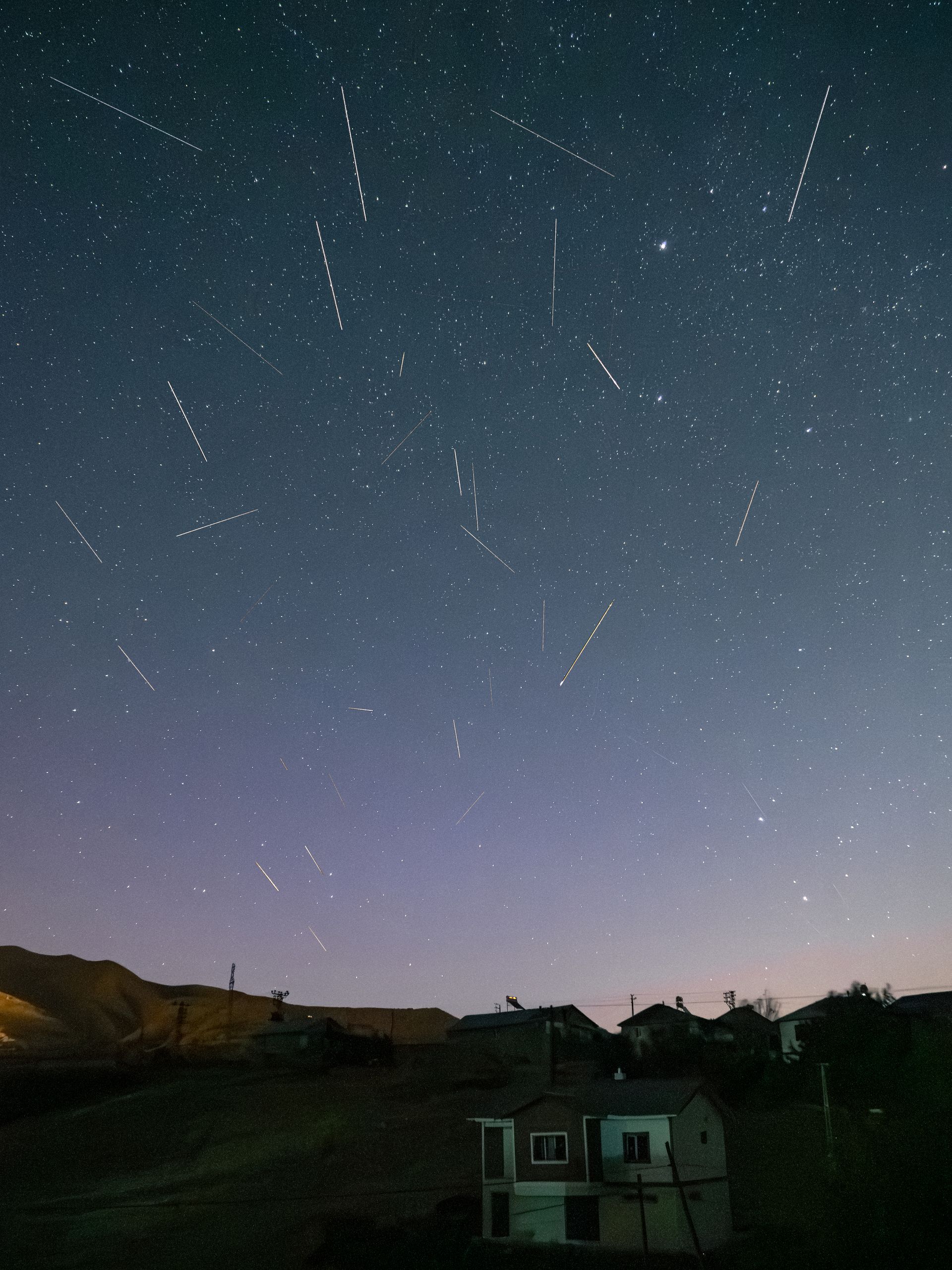 A mesmerizing view of a meteor shower illuminating the night sky over a quiet mountain village.