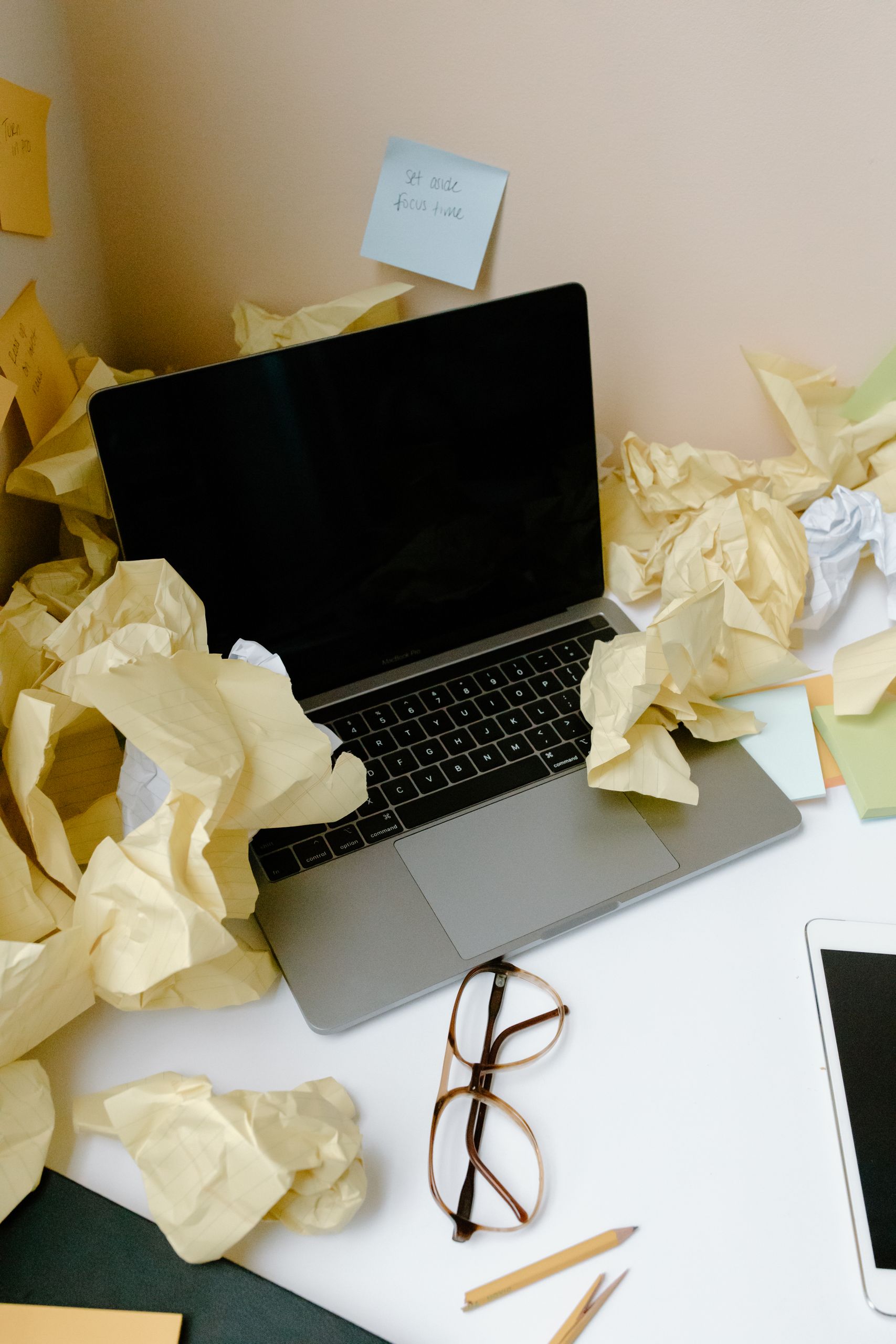 A messy desk covered with crumpled papers and a laptop reflecting disorganization.