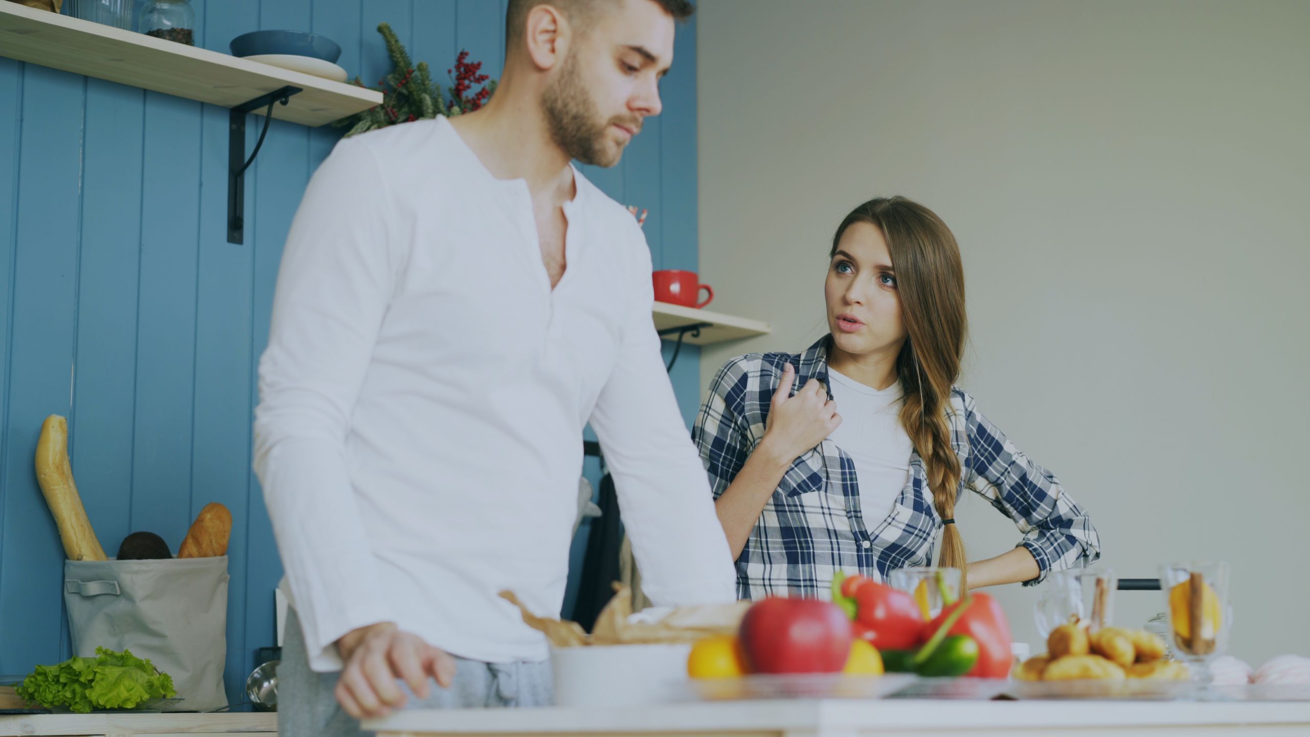A young couple discussing in a kitchen with fresh vegetables on the counter.