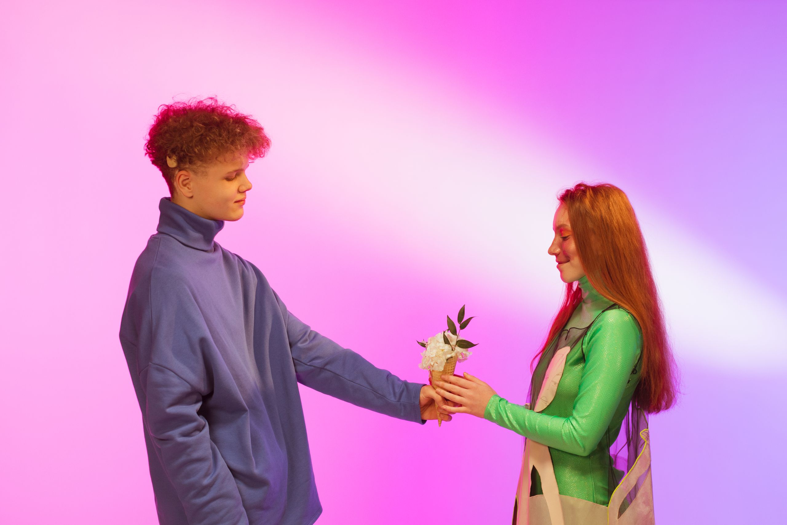 A young couple in a studio exchanging flowers on a colorful background.