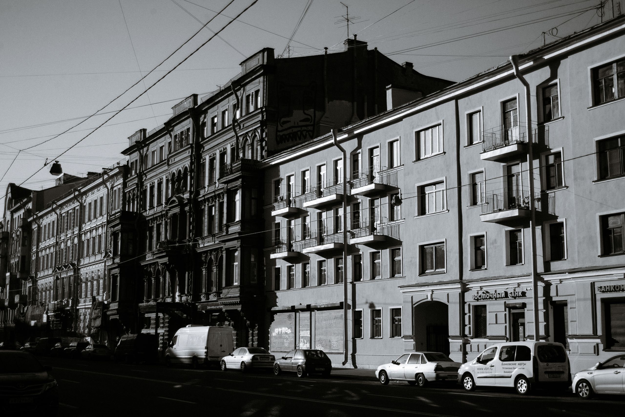 Black and white of aged residential buildings with parked cars located in Saint Petersburg Russia on sunny day
