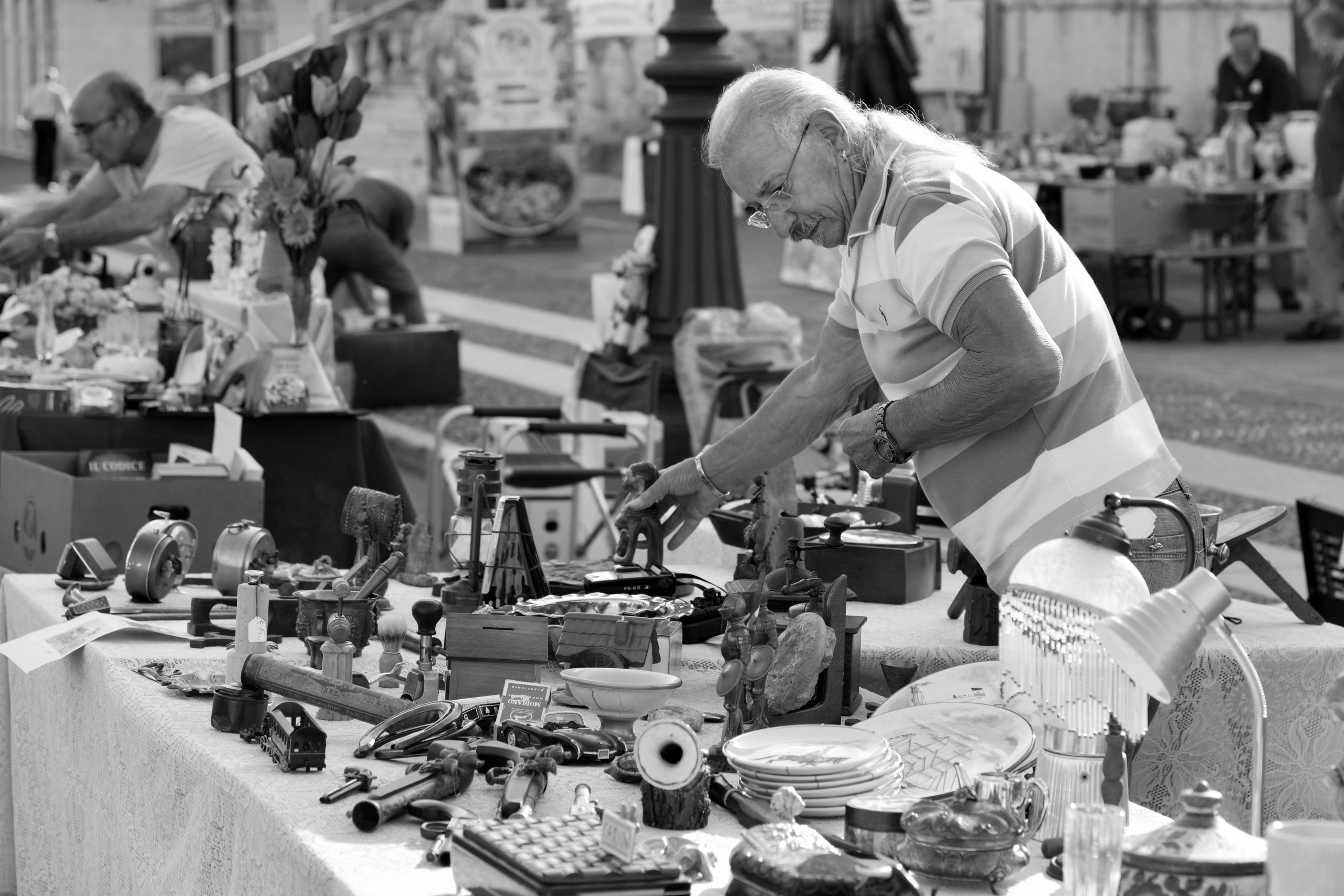 Black and white photo of an elderly man browsing items at a street market in Villafranca di Verona, Italy.