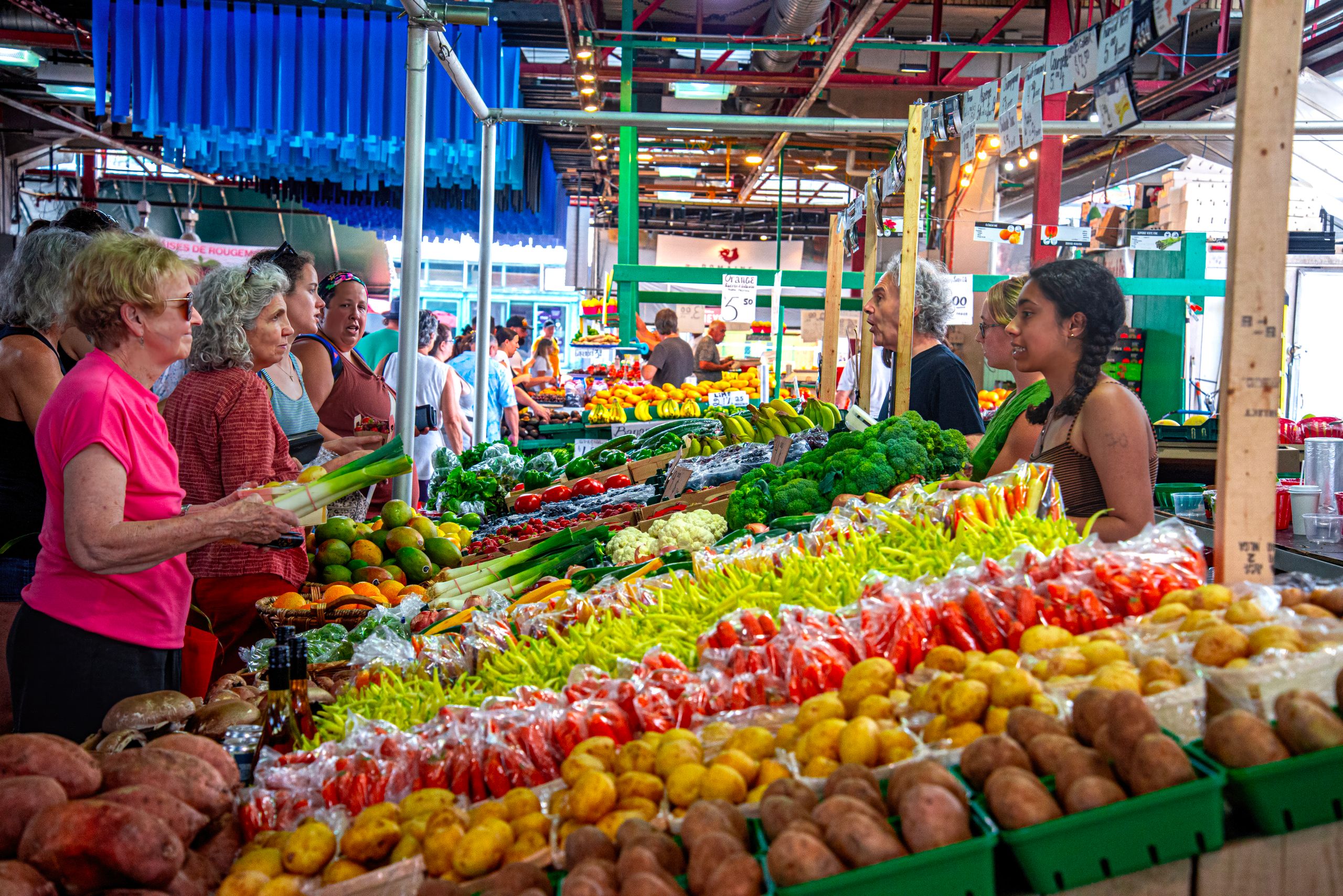 Bustling street market scene with diverse people buying fresh vegetables and fruits.