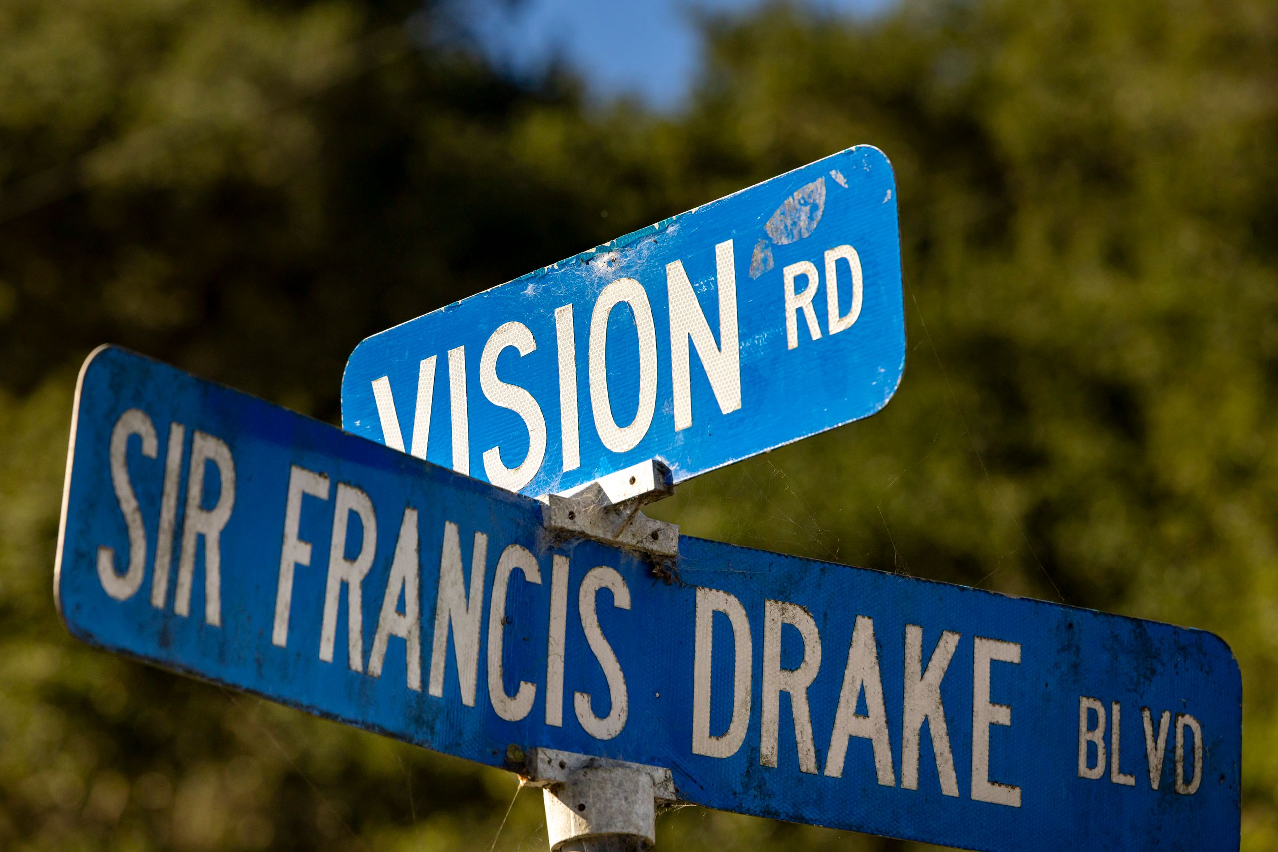Close-up of intersecting street signs for Vision Rd and Sir Francis Drake Blvd against a green background.