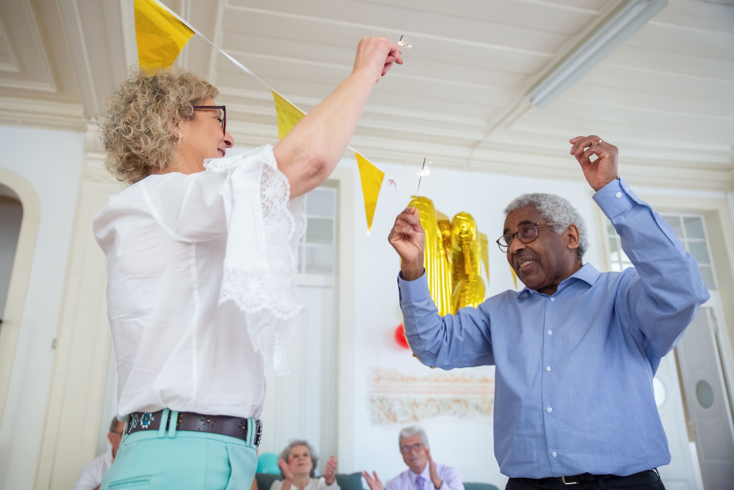 Elderly friends celebrate with sparklers indoors, enjoying a joyful moment together.