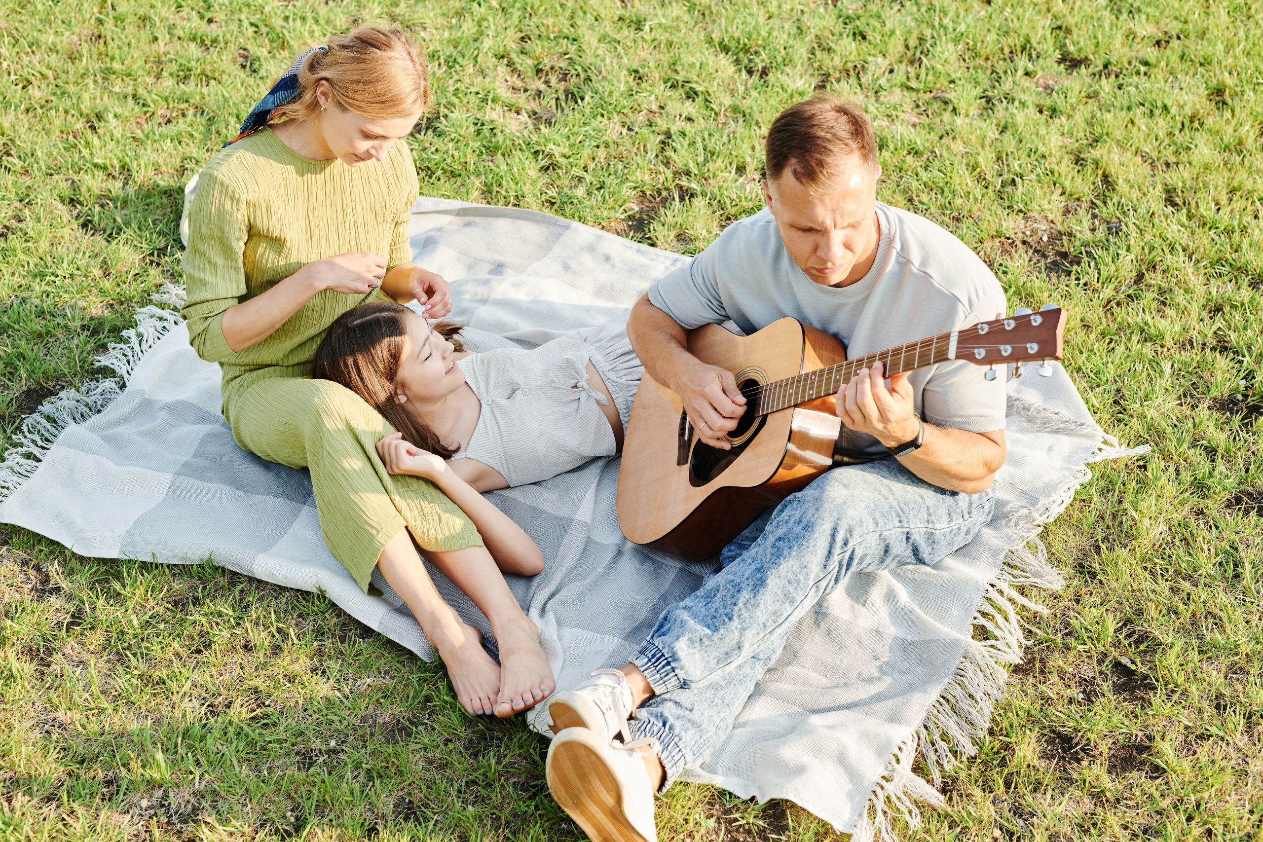 Family enjoying a relaxing picnic with guitar music on a sunny day outdoors.