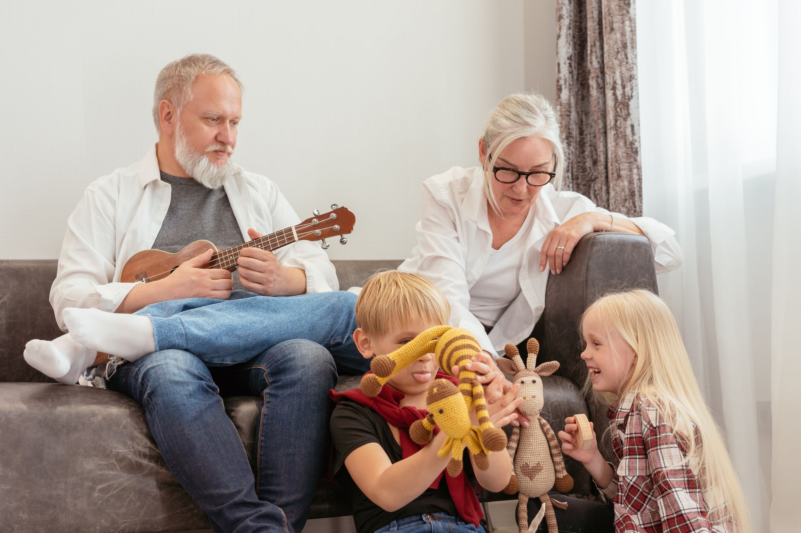 Grandparents enjoying time with grandchildren indoors, playing with ukulele and toys.