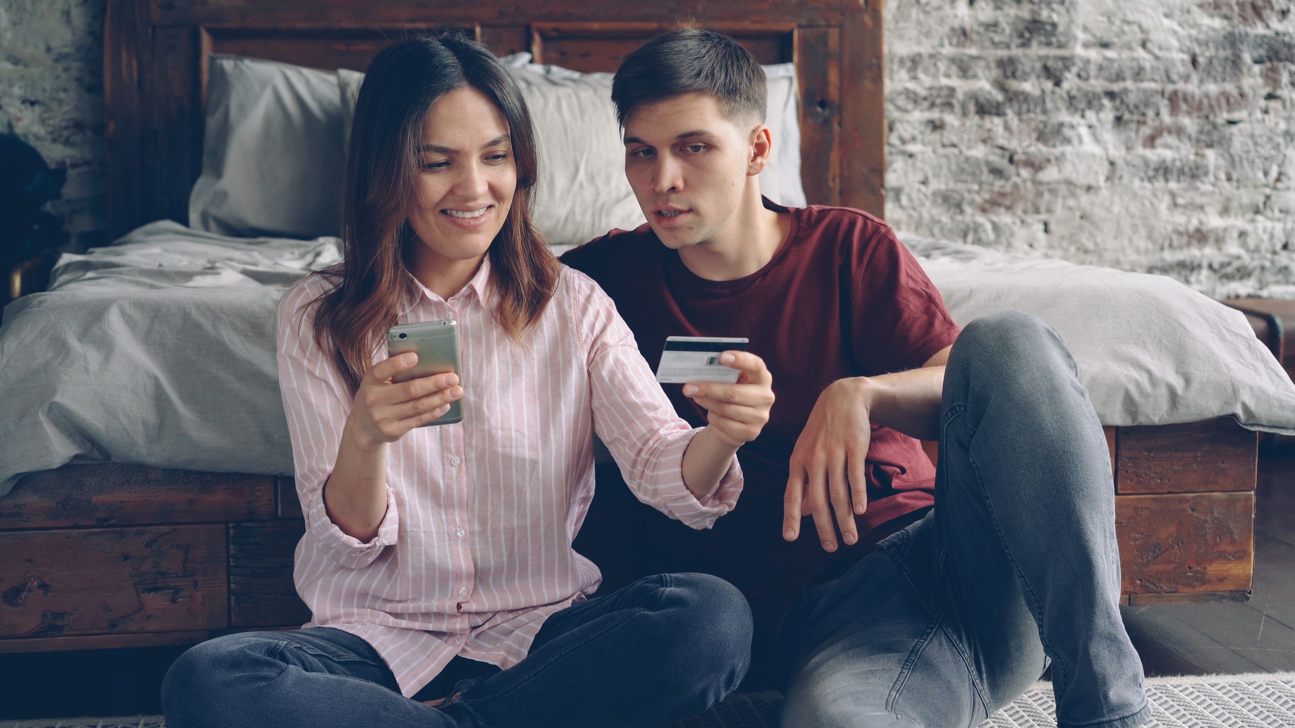 Happy couple using a smartphone and credit card for online shopping at home.