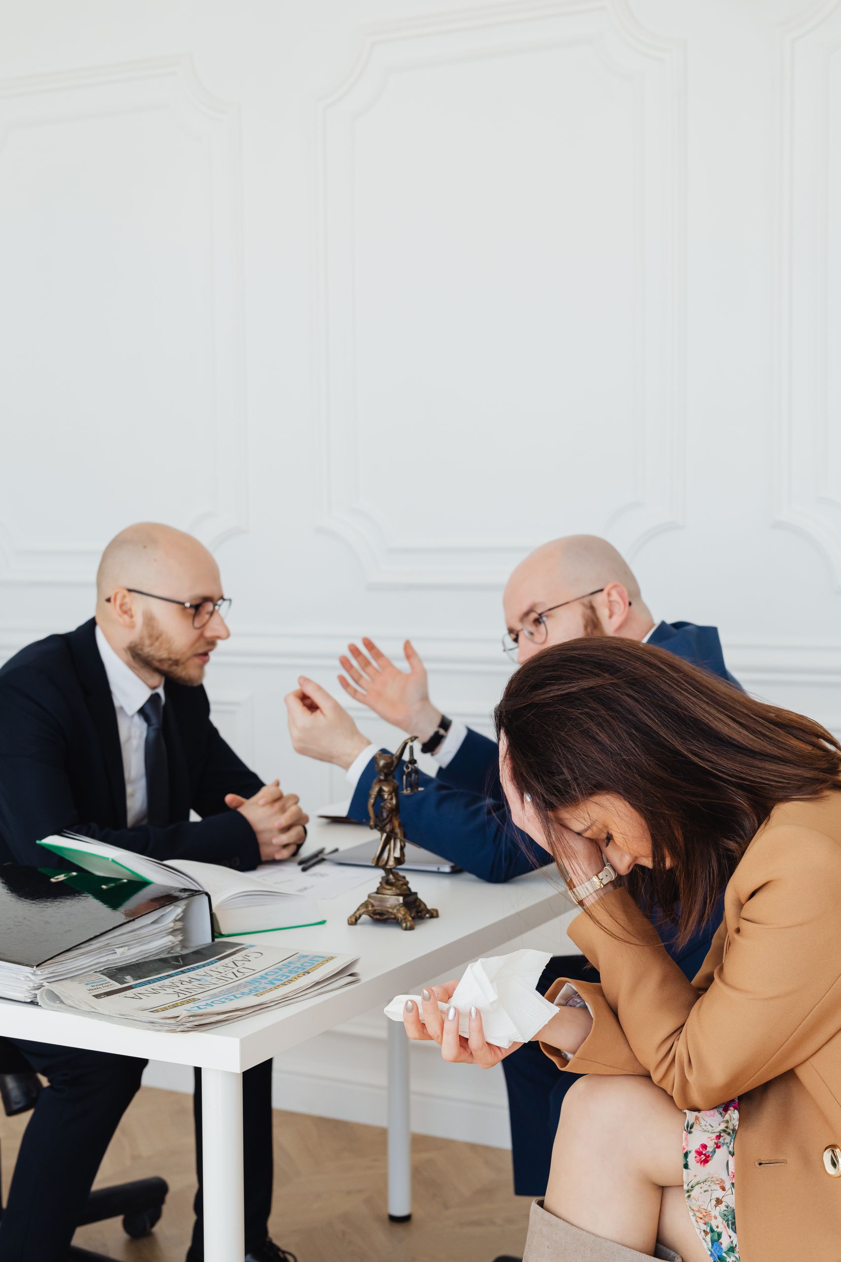 Intense legal discussion between two men and a distressed woman in an office setting with Lady Justice statue.