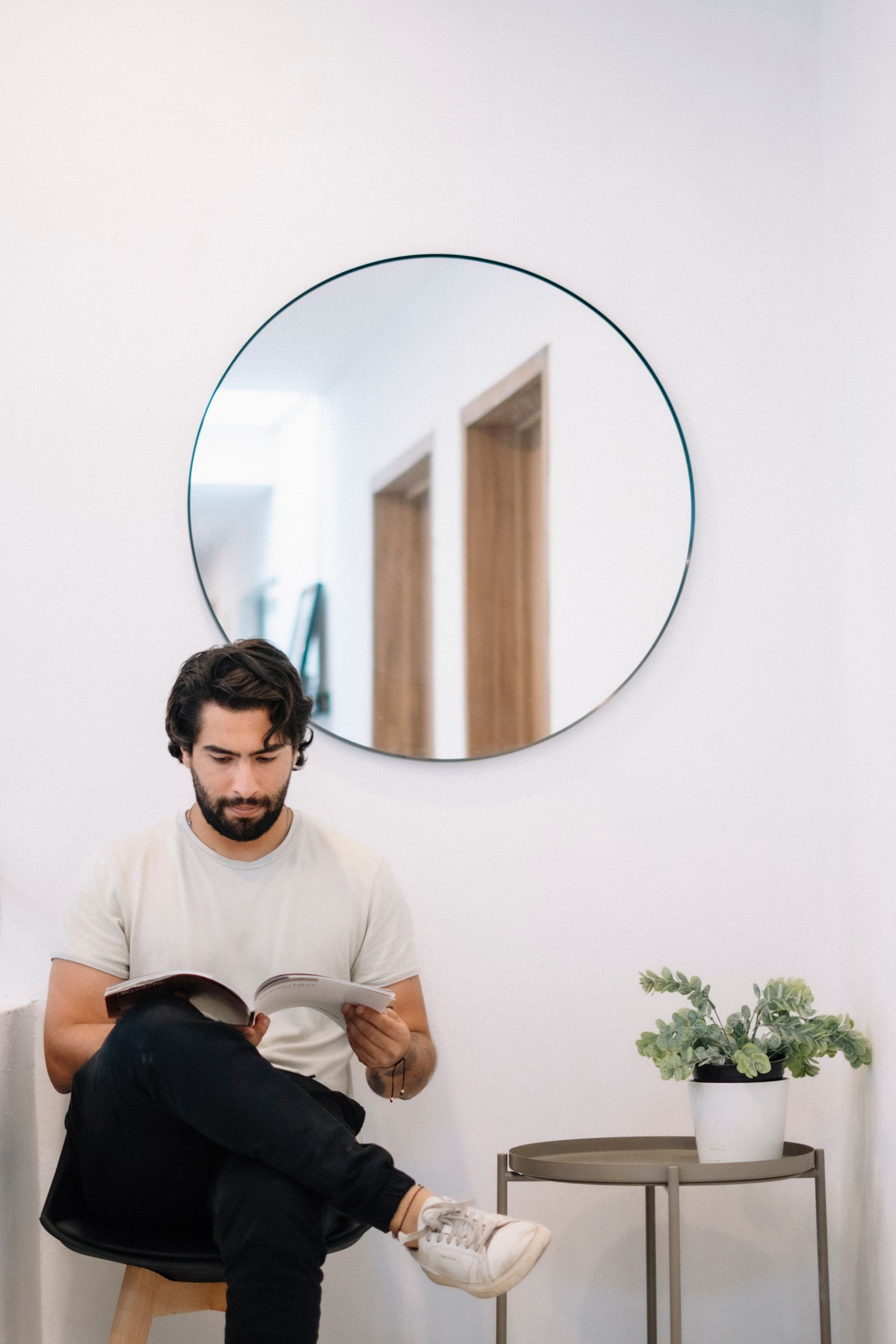 Man reading in a modern minimalist room with a circular mirror and potted plant.