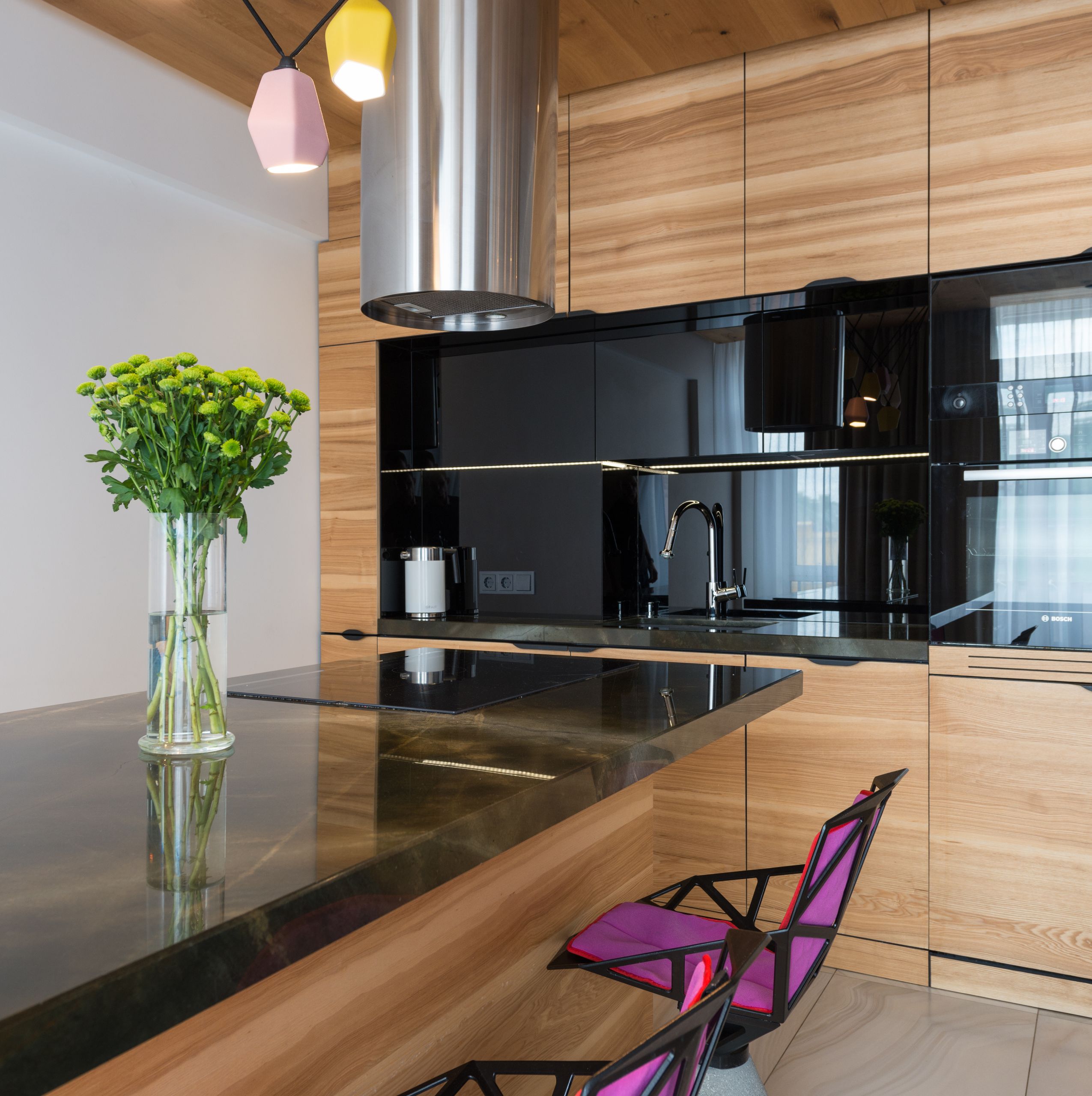 Modern kitchen interior design with contemporary built in appliances and counter decorated with creative chandelier and cozy chairs