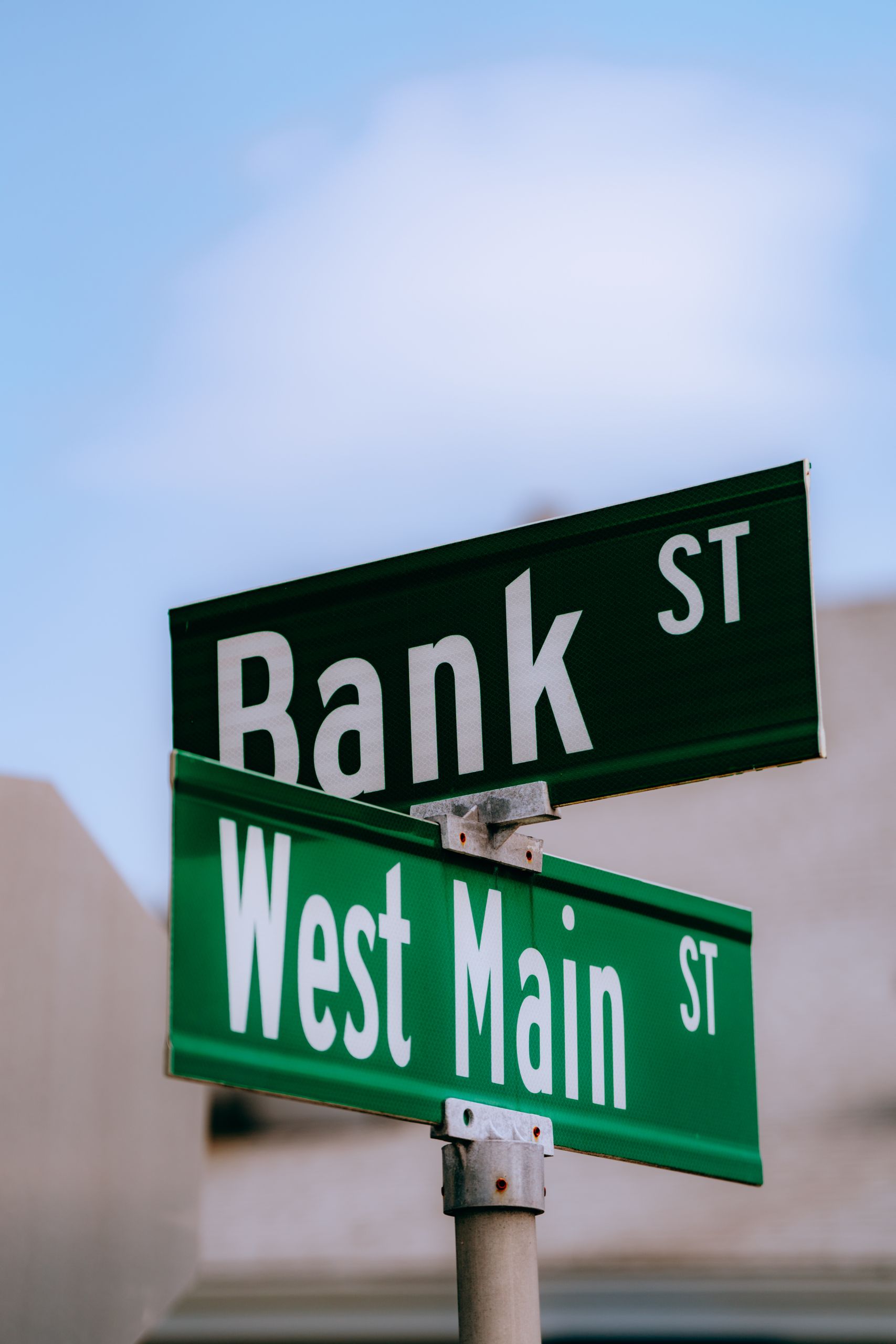 Street signs at the intersection of Bank St and West Main St, clear blue sky background.