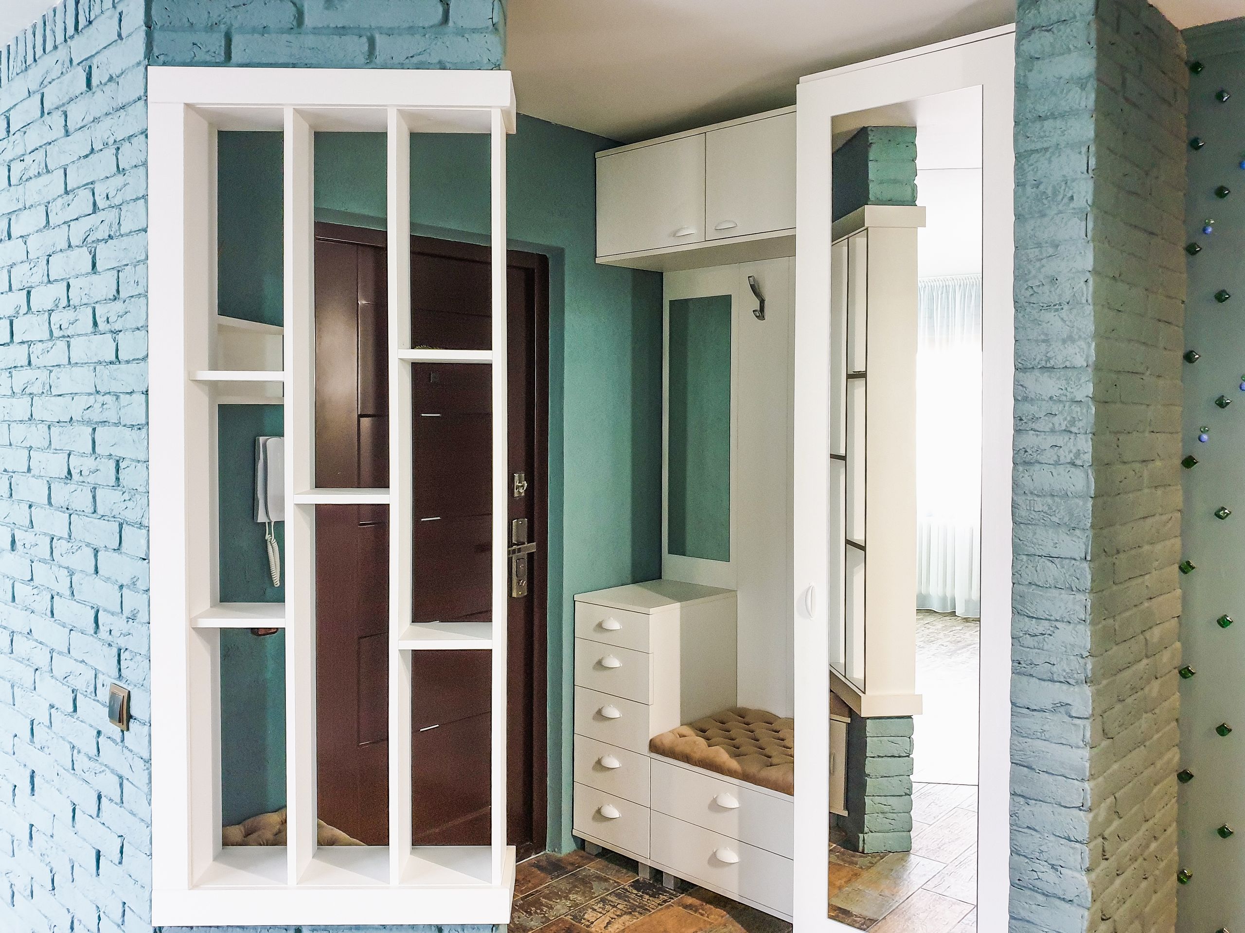 Stylish modern entryway with white shelving and brick walls in a home interior.