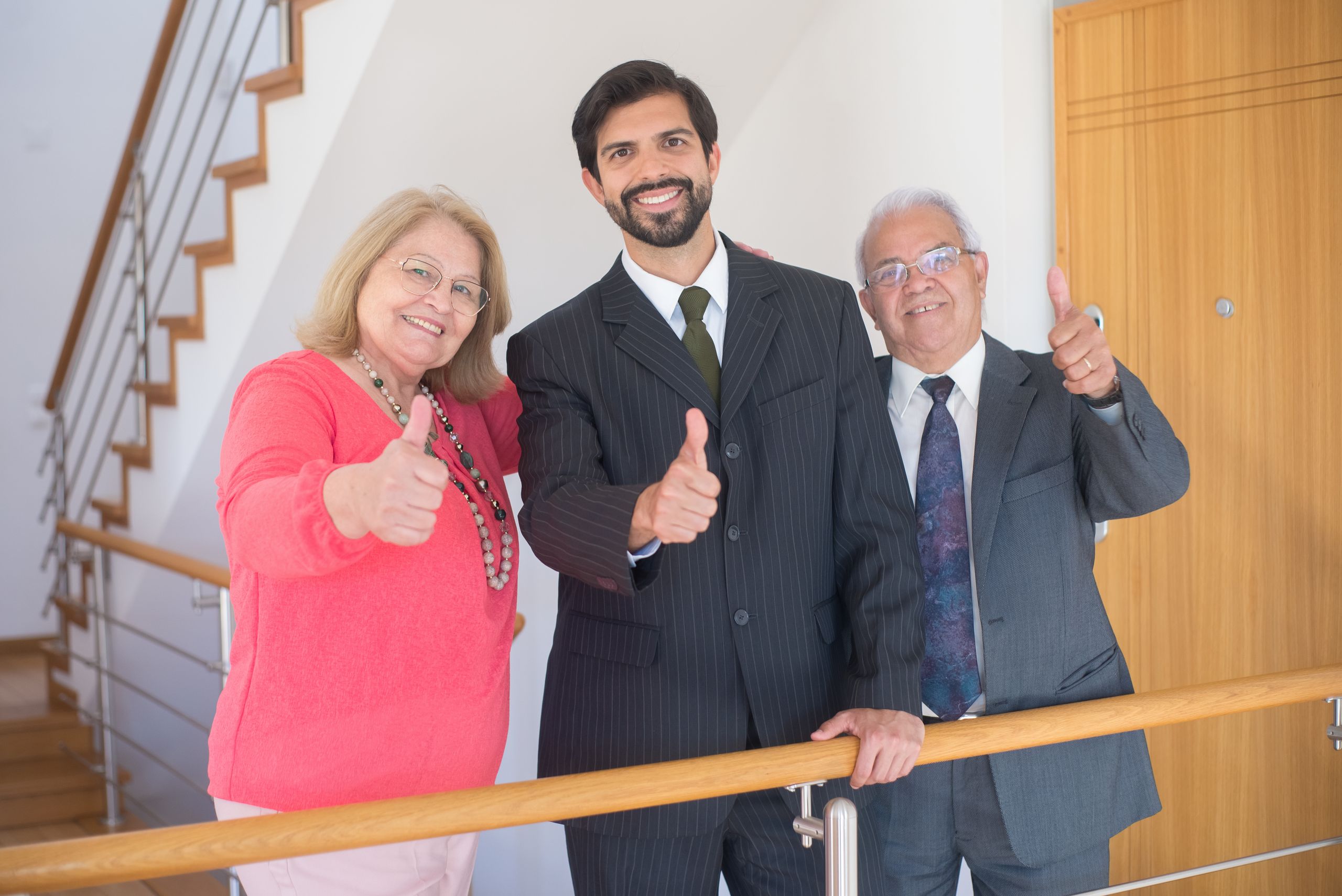 Three business professionals giving thumbs up in an indoor setting, symbolizing success and agreement.