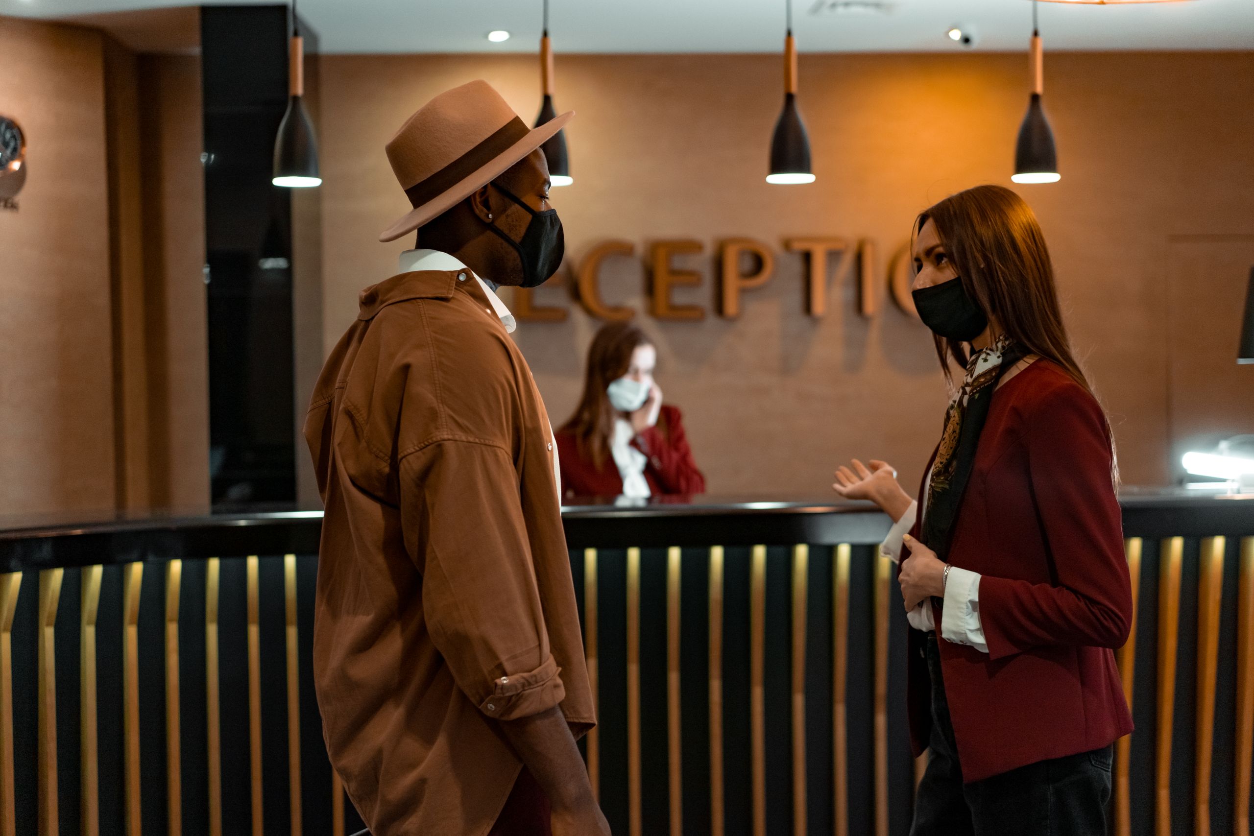 Two people in face masks interacting at a hotel reception desk during the COVID-19 pandemic.
