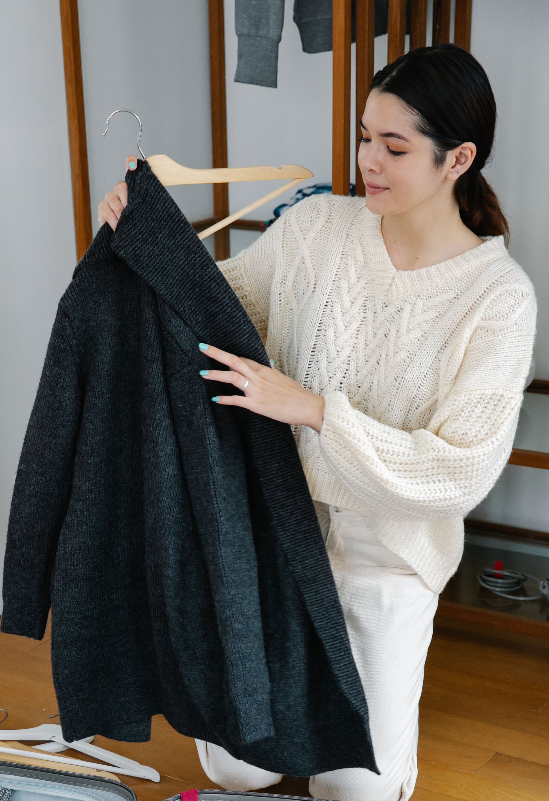 Woman organizing a black coat and sweater in a wardrobe indoors.
