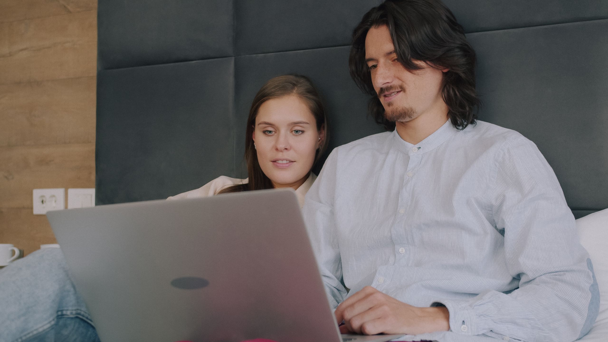 Young couple relaxing on bed using a laptop for online browsing or streaming.