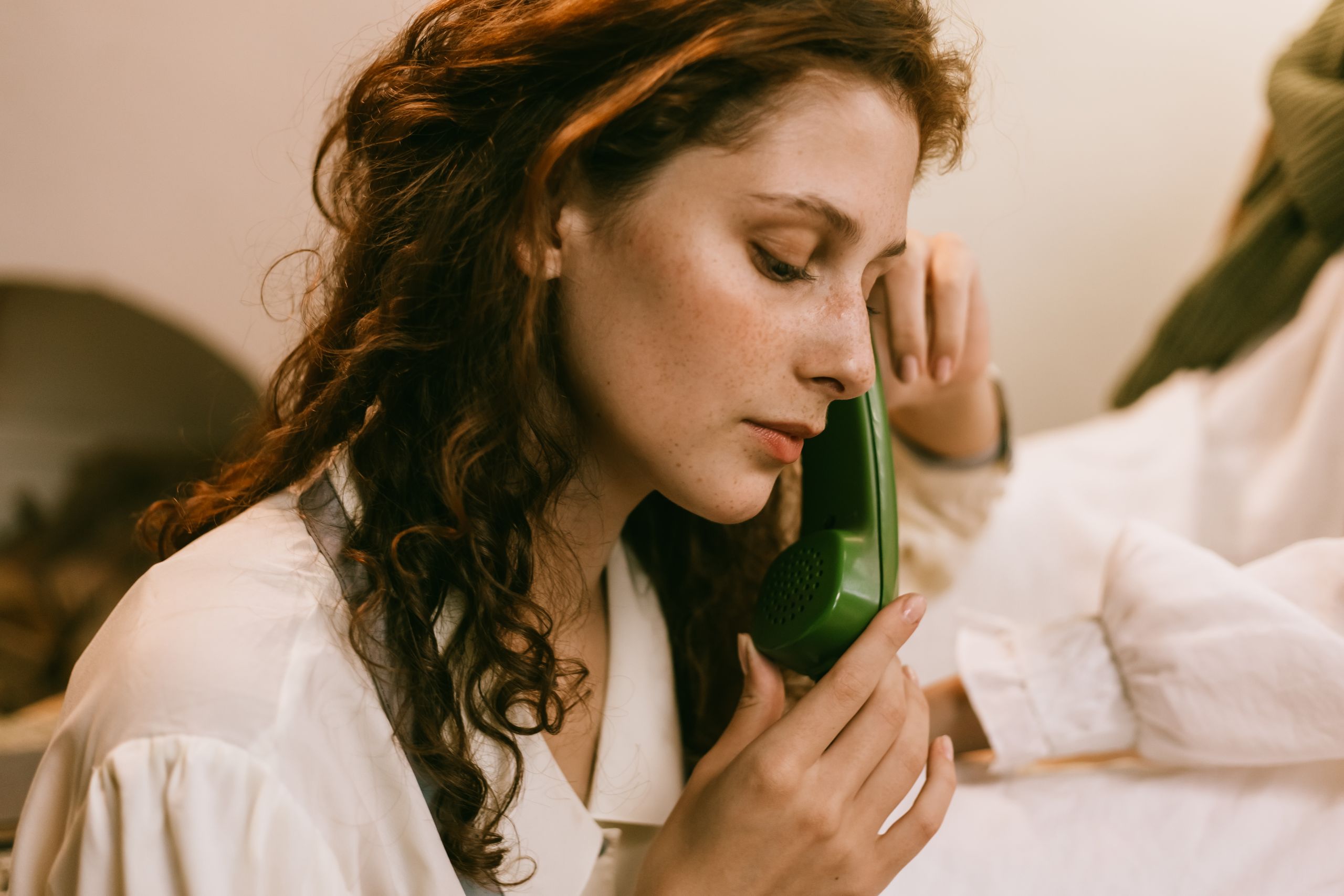 Young woman with red curly hair using a vintage green telephone. Indoor setting, soft light.