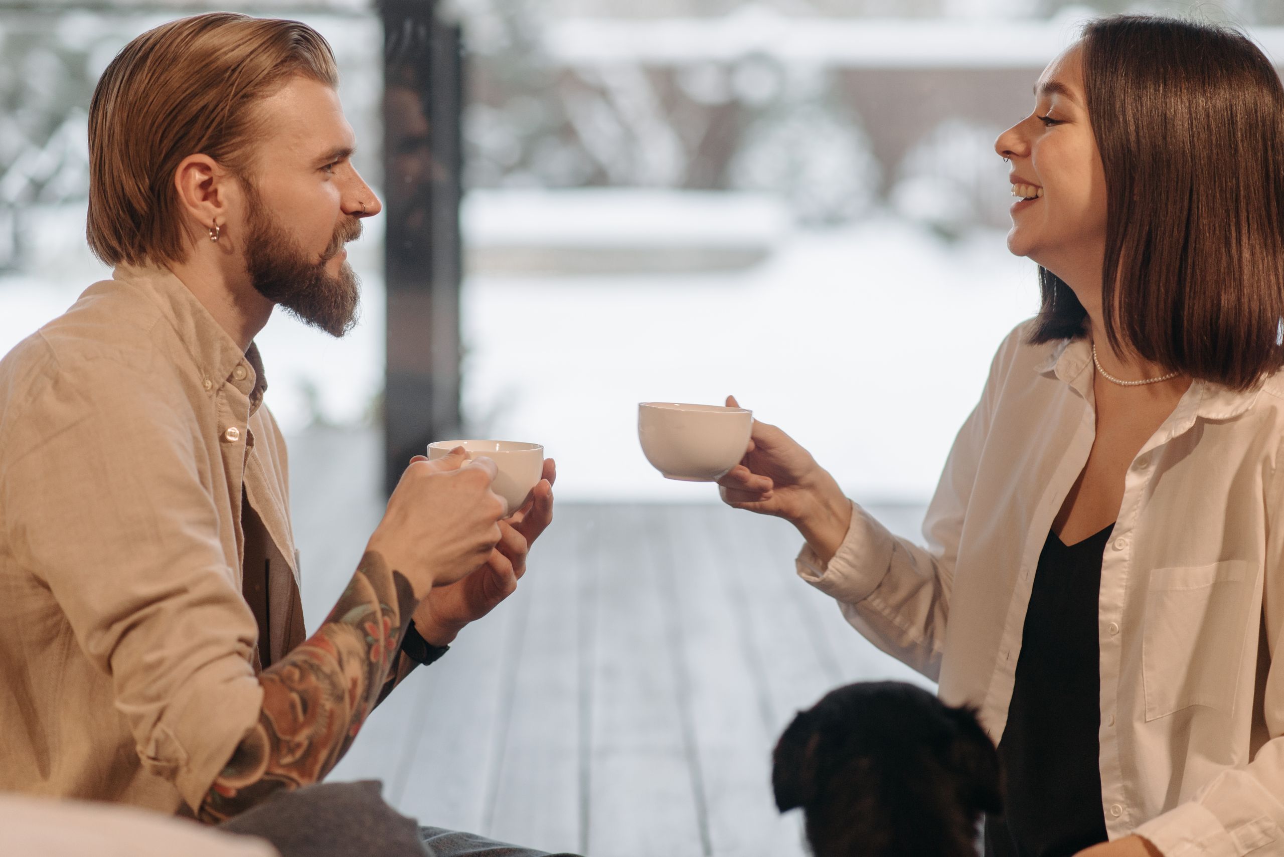 A cheerful couple sits indoors, enjoying a warm coffee together with a smile.