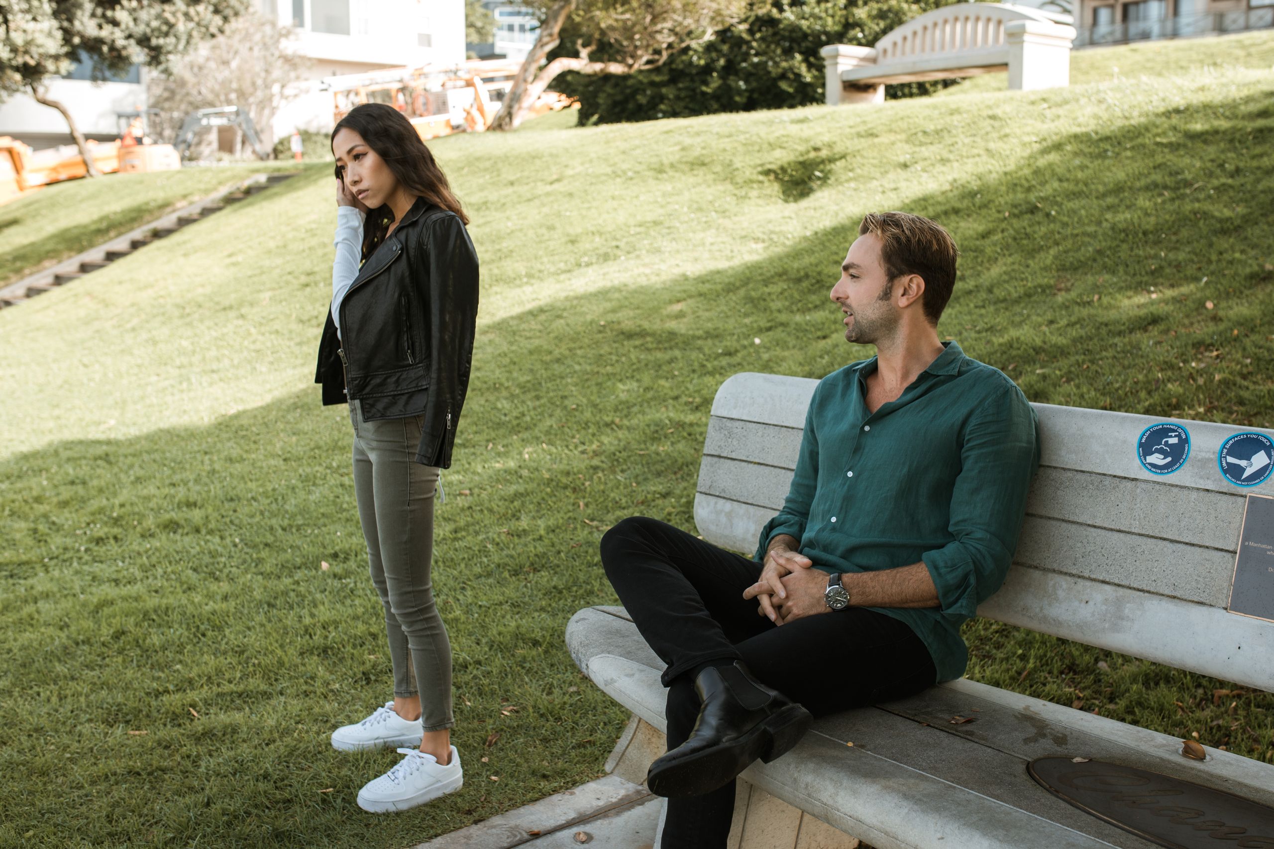 A couple having a disagreement on a park bench in a grassy outdoor setting.