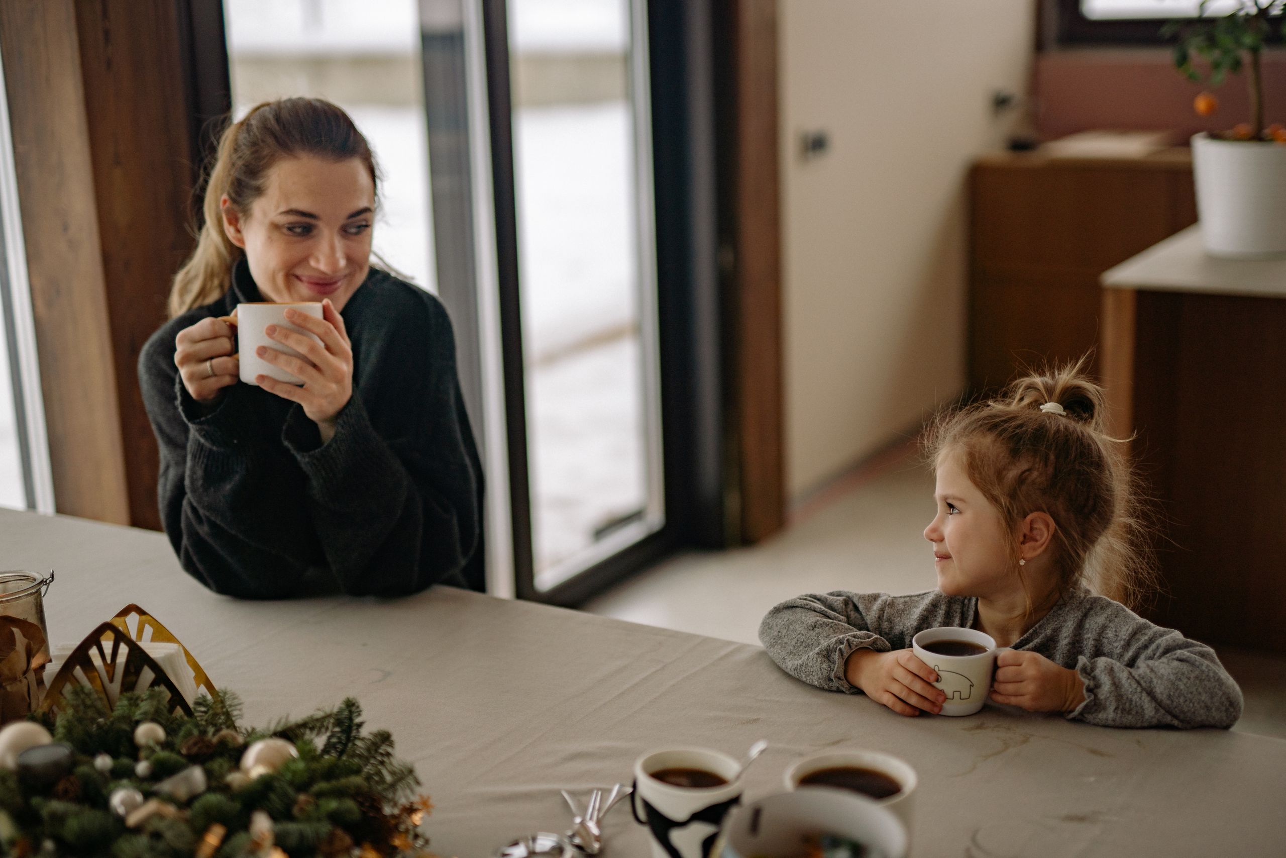 A heartwarming scene of a mother and daughter bonding over coffee at home, with a cozy holiday atmosphere.