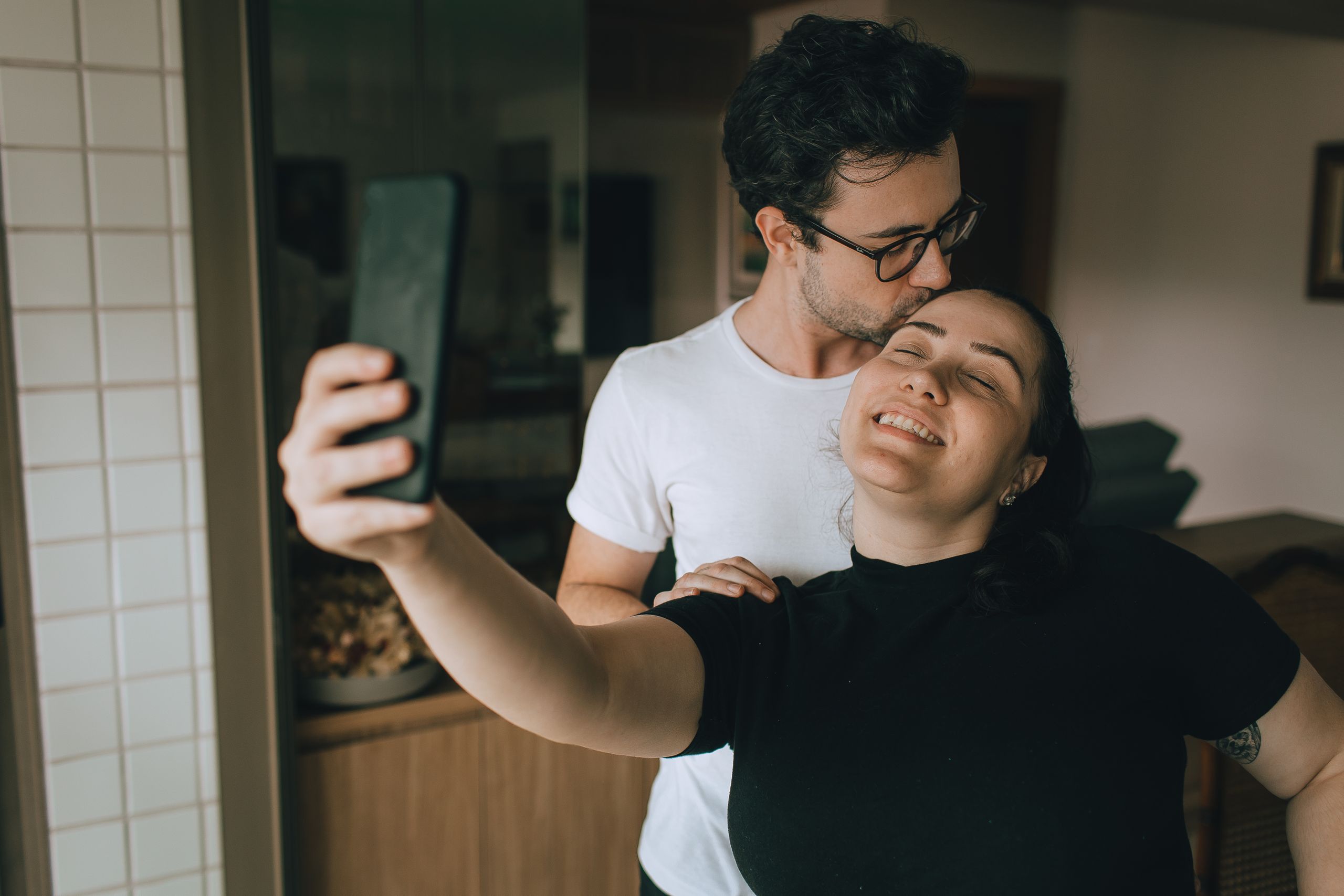 A joyful couple capturing a selfie moment indoors, showcasing affection and happiness.