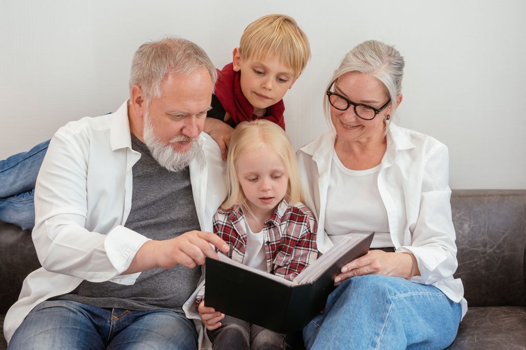 Grandparents and grandchildren reading a photo album on the couch, embracing family bonds and love.